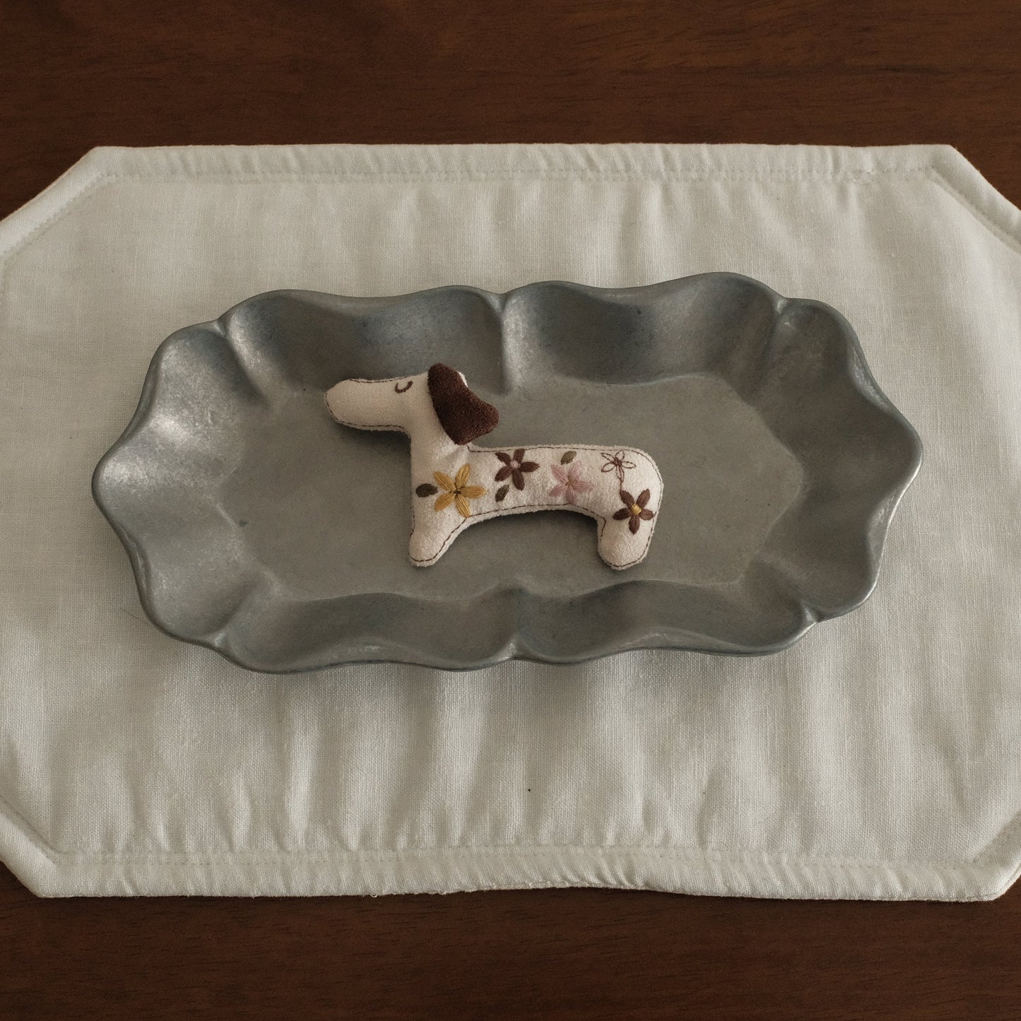Decorative dachshund dog figurine brooch on a grey metal dish plate with a white placemat