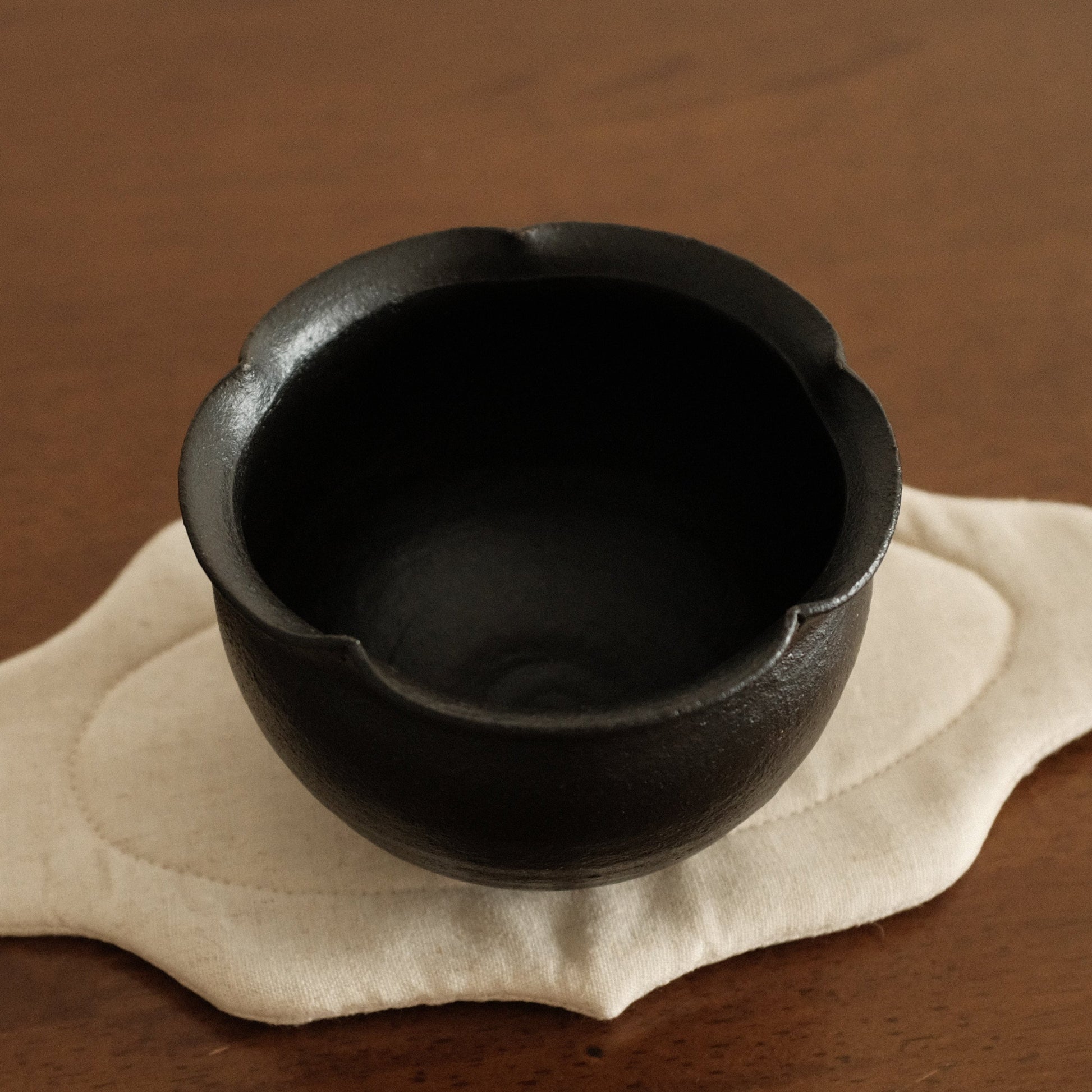 Black ceramic cup on a beige coaster with a brown background