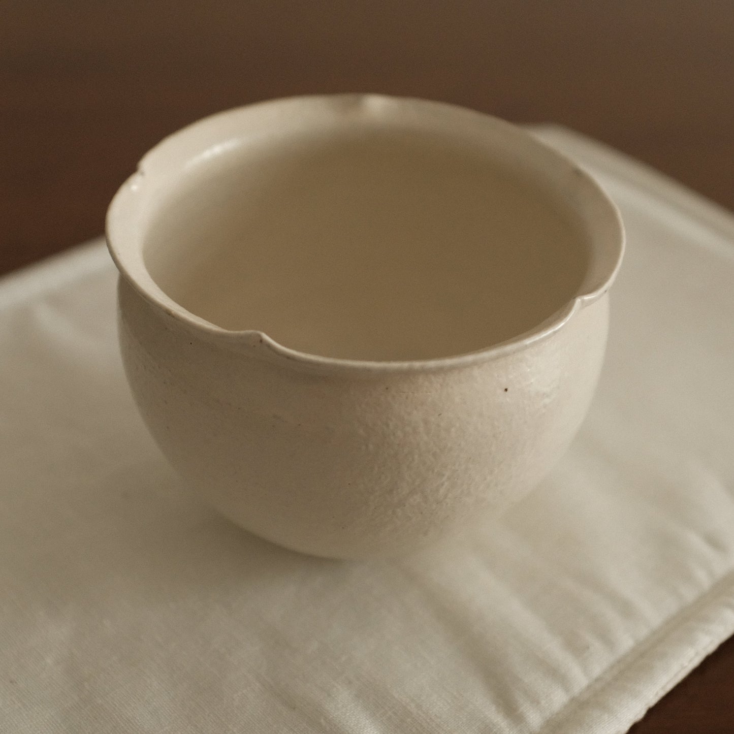 White ceramic floral rim cup on a textured white surface with a brown