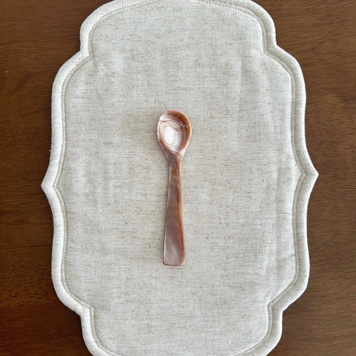 Decorative white placemat with a small decorative spoon on a wooden surface