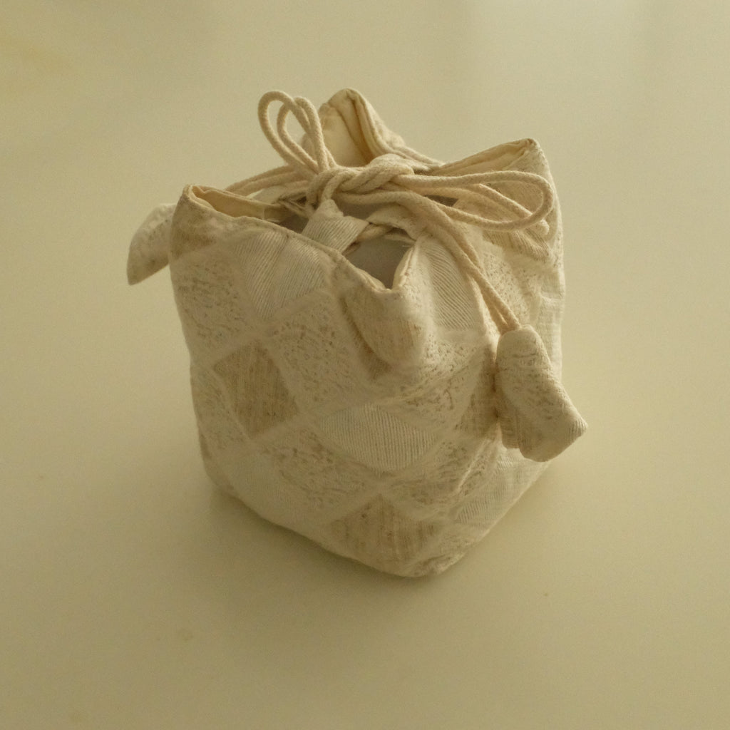 A small beige fabric drawstring pouch with a textured, woven pattern, photographed on a plain beige background.