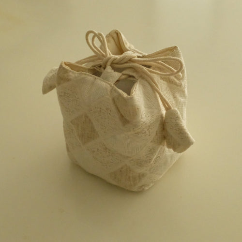 A small beige fabric drawstring pouch with a textured, woven pattern, photographed on a plain beige background.