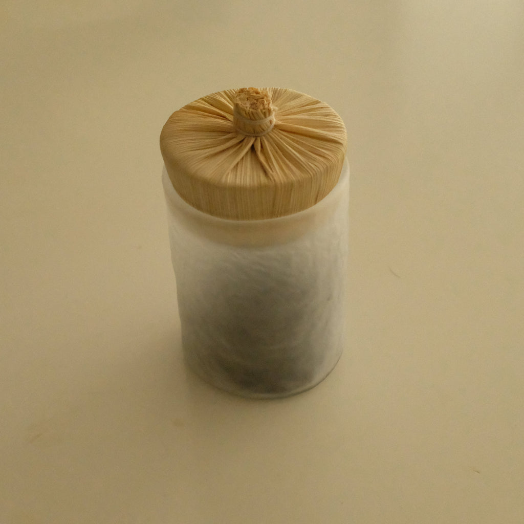 A small cylindrical container with a light wood-grain bamboo lid, filled with white tea leaves, set against a plain beige background.
