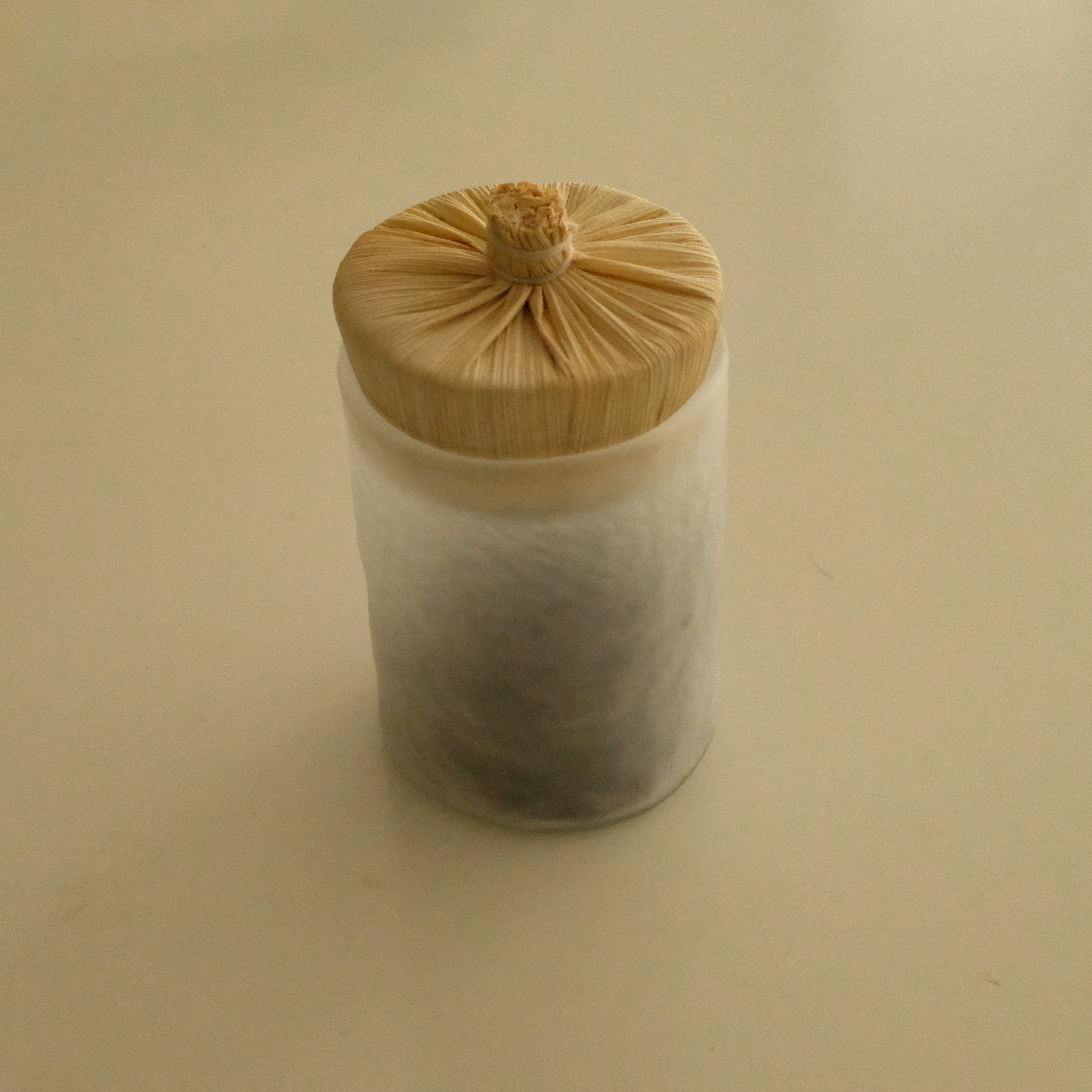 A small cylindrical container with a light wood-grain bamboo lid, filled with white tea leaves, set against a plain beige background.