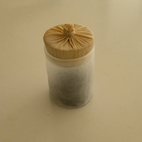 A small cylindrical container with a light wood-grain bamboo lid, filled with white tea leaves, set against a plain beige background.