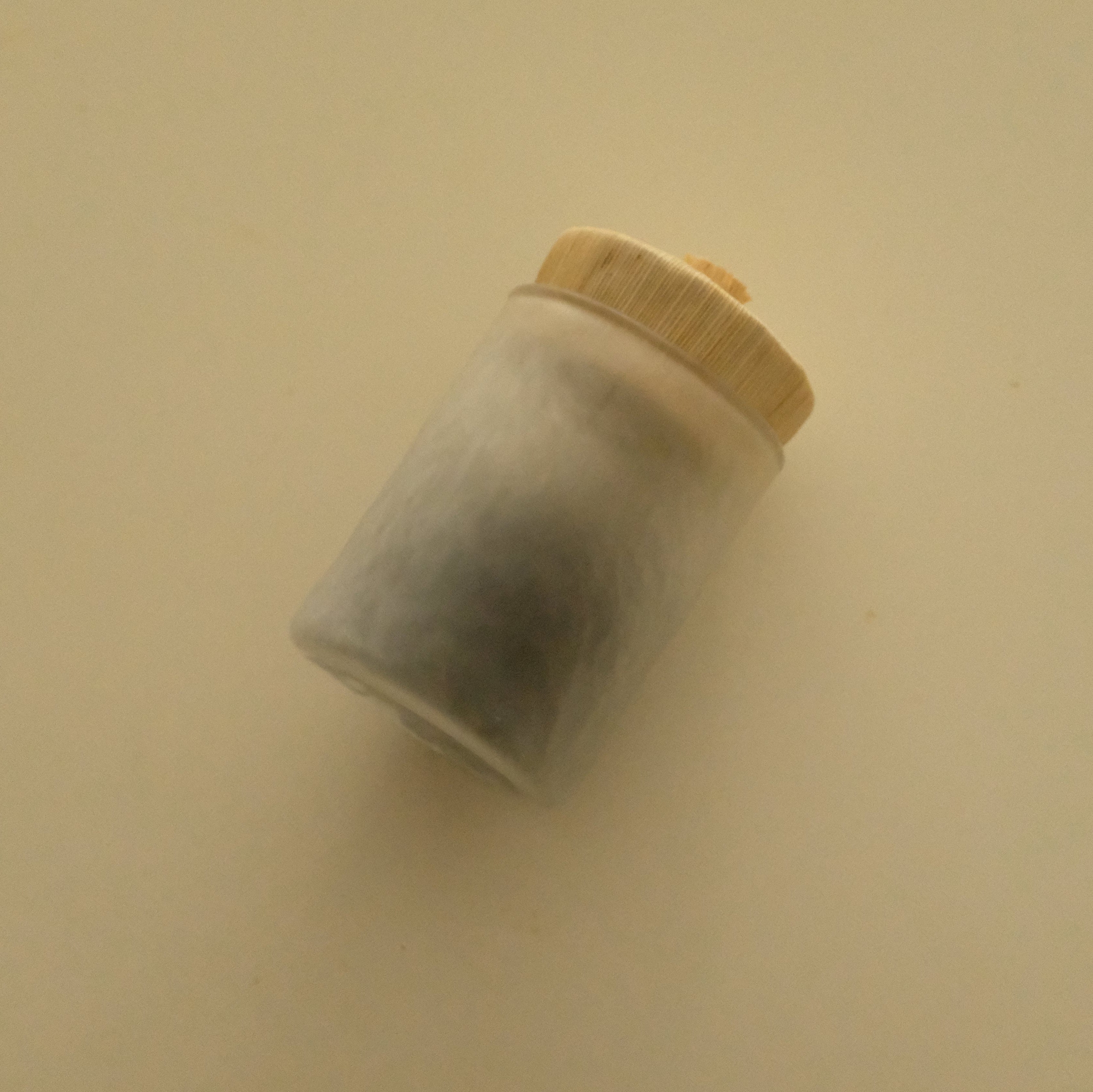 A small translucent frosted glass jar with a light beige wooden lid, shown on a plain beige background.