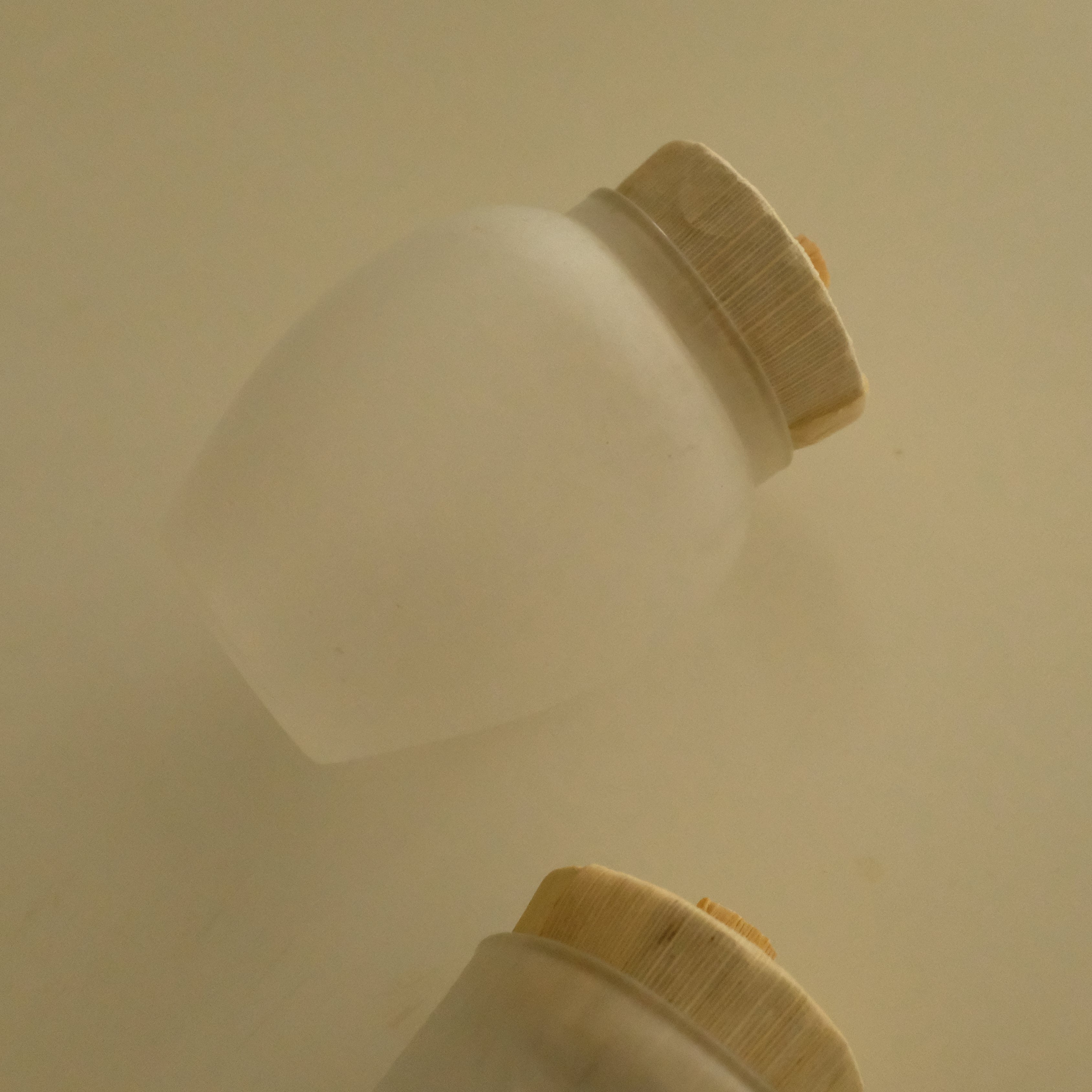Two frosted glass cosmetic bottles with beige screw caps, shown on a plain beige background.