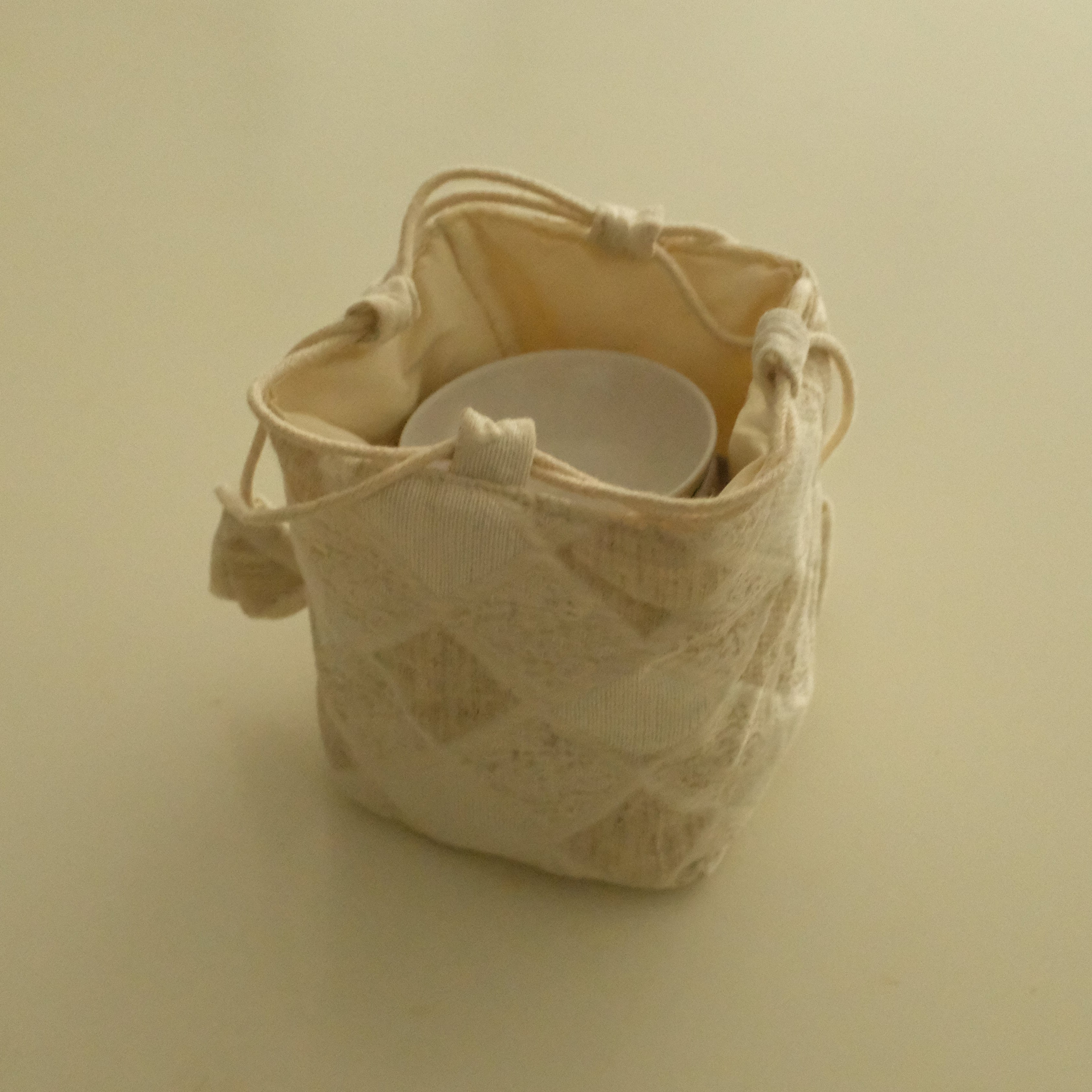 A small cream-colored fabric drawstring pouch with a subtle woven pattern, shown on a plain beige background.