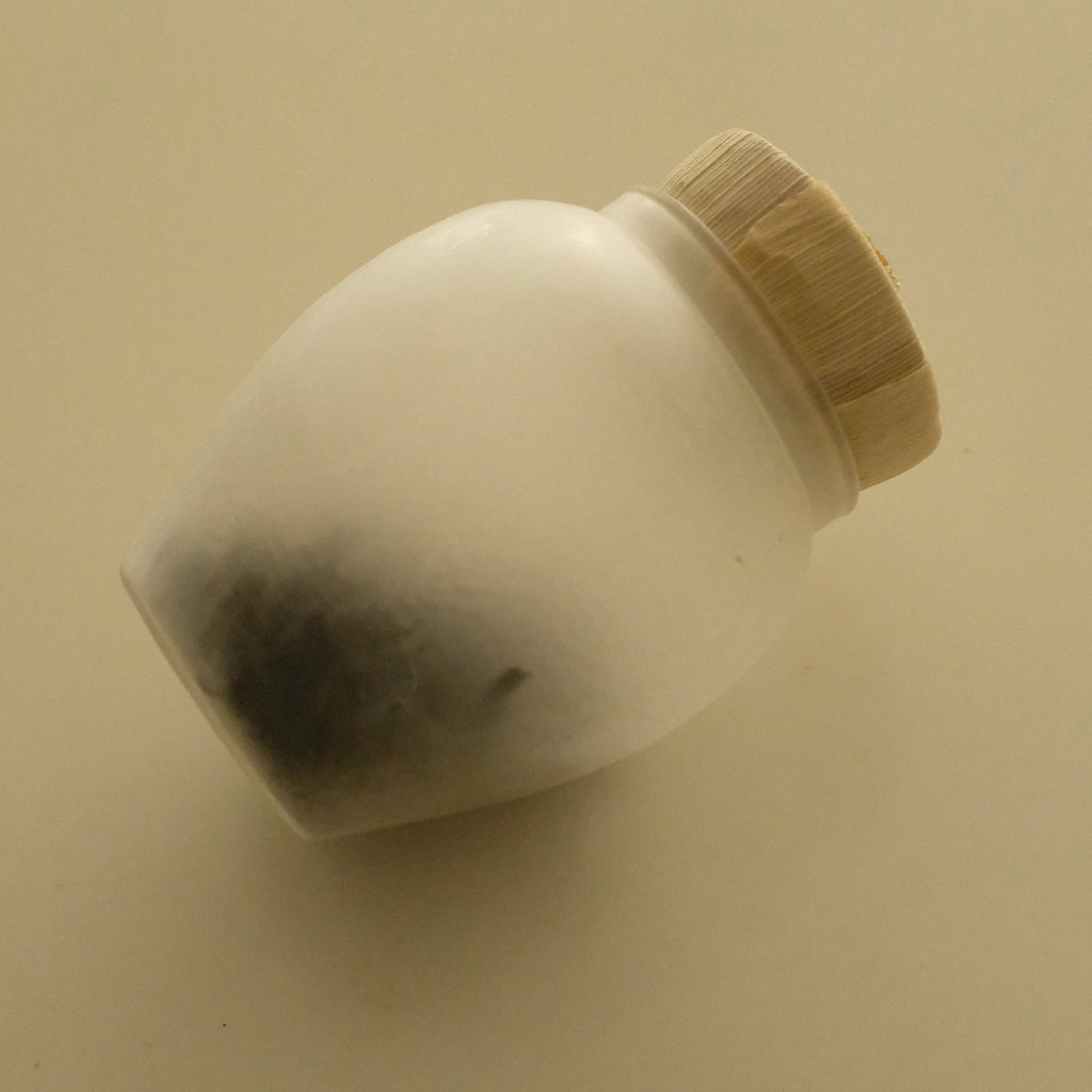A small white ceramic jar with a light wood-grain textured lid, photographed on a plain beige background.