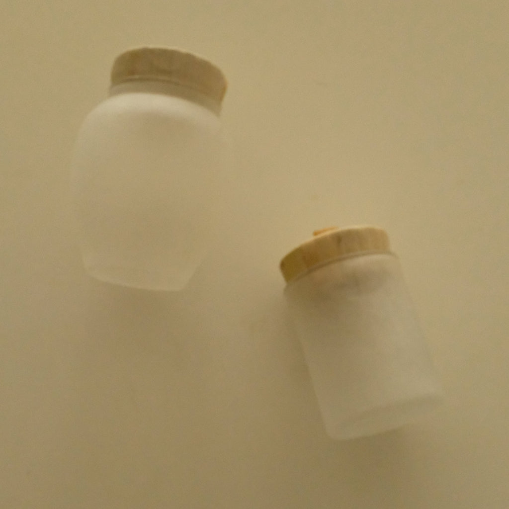 Two frosted glass travel bottles with cork stoppers, shown on a plain beige background.