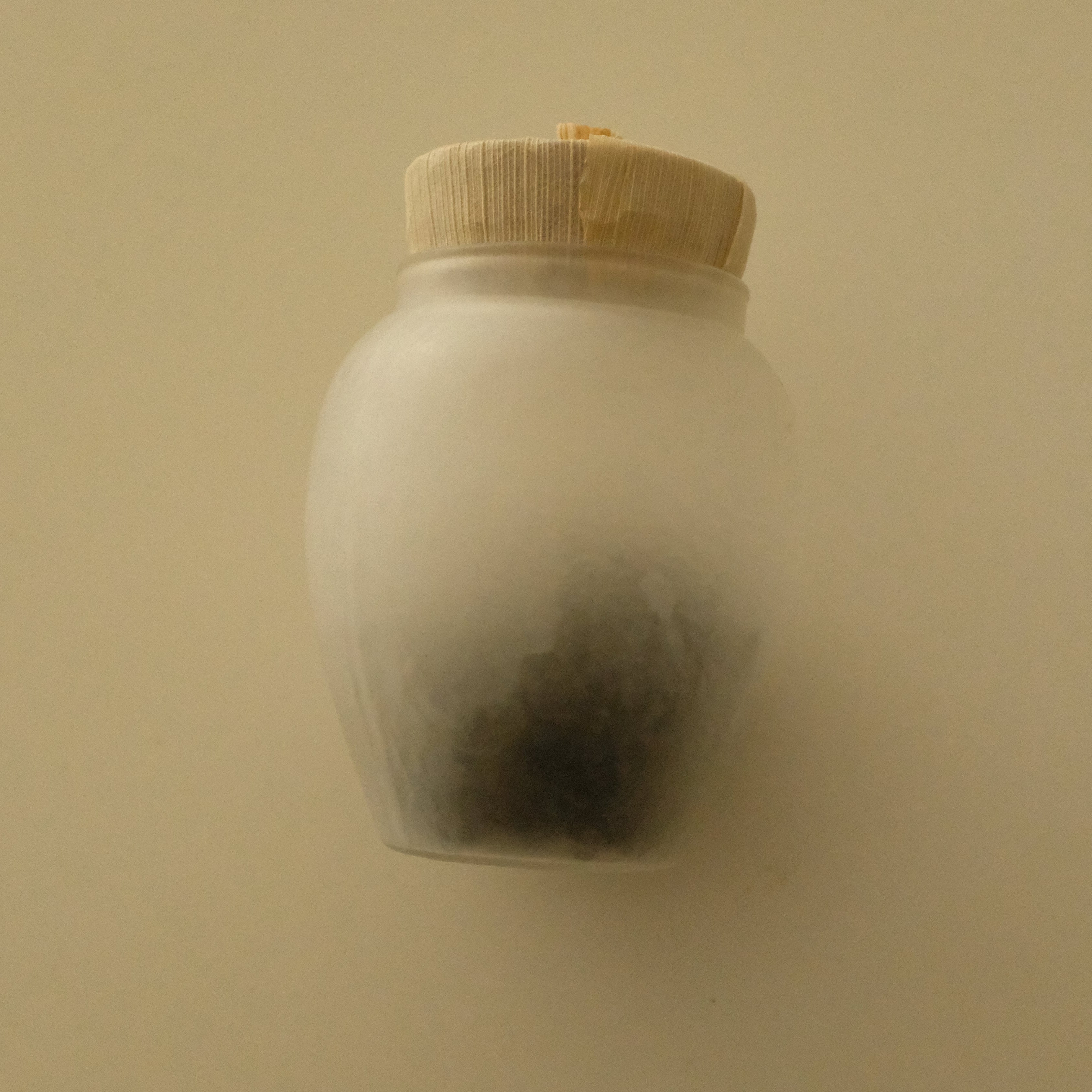 A small frosted glass jar with a light beige bamboo lid, shown against a plain beige background.