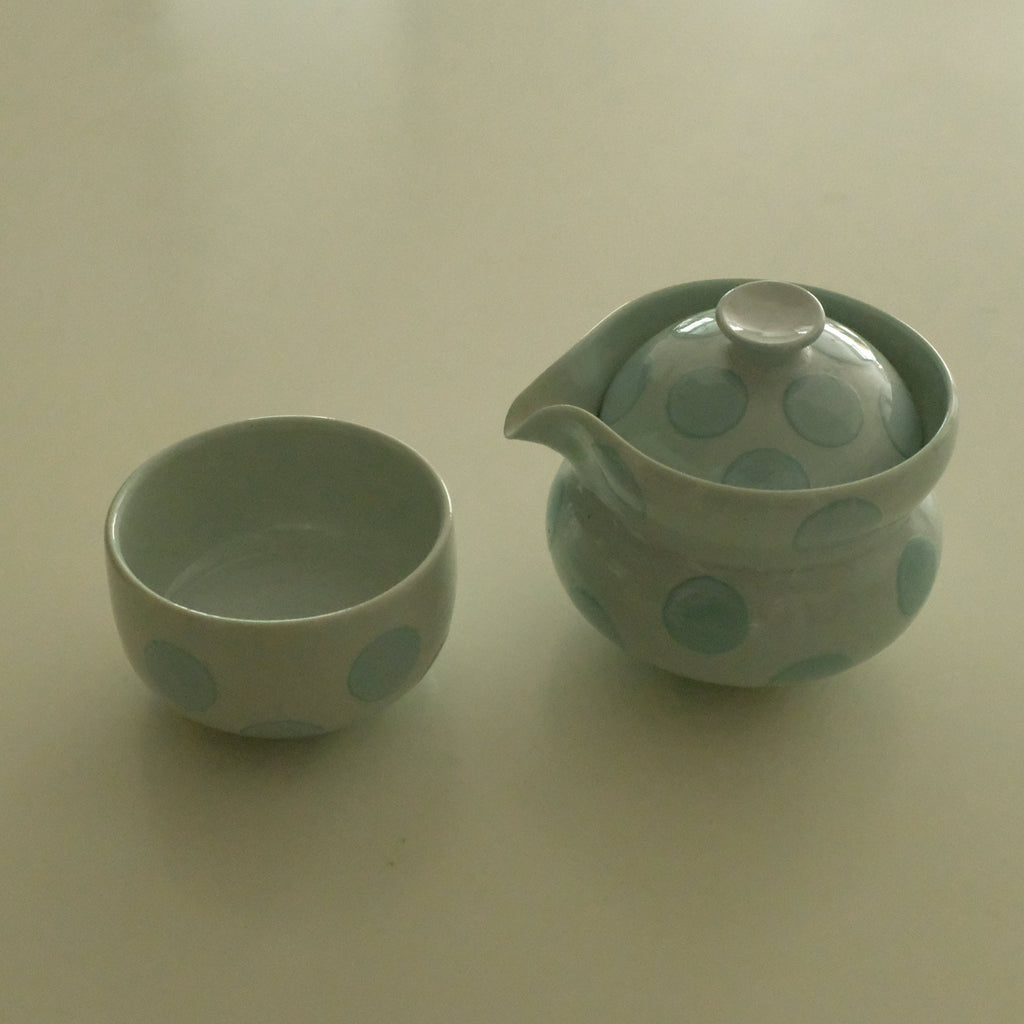 A small ceramic teapot and matching cup set in a pale mint green color with darker green polka dots, set against a plain off-white background.