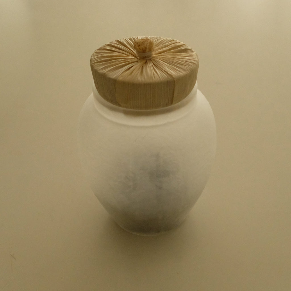 A frosted glass jar with a light natural wood lid, photographed on a plain beige background.