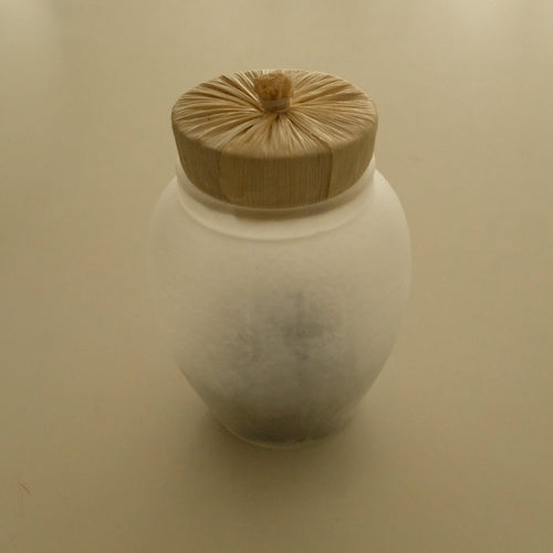 A frosted glass jar with a light natural wood lid, photographed on a plain beige background.
