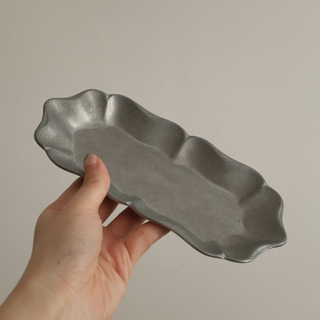Hand holding a gray metal dish against a plain background