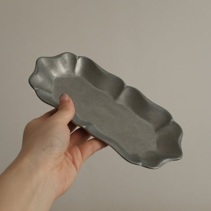 Hand holding a gray ceramic dish against a plain background