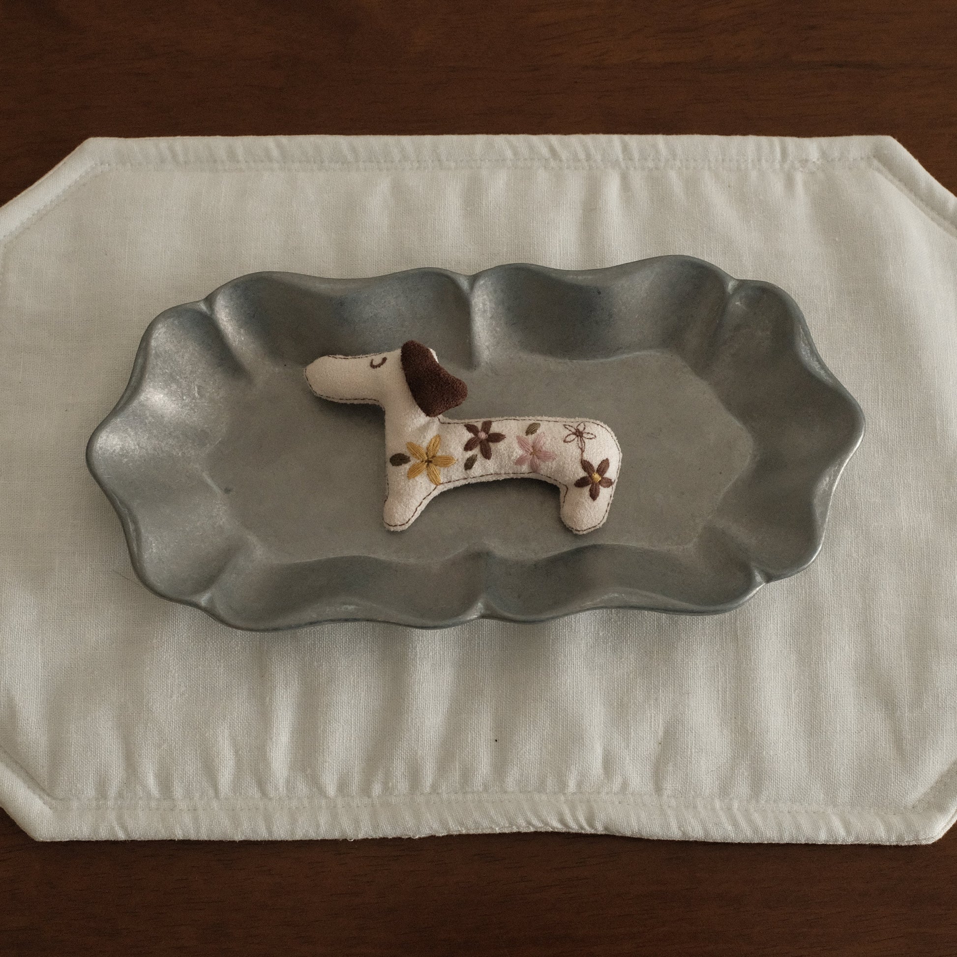 Decorative dachshund dog figurine brooch on a grey metal dish plate with a white placemat 