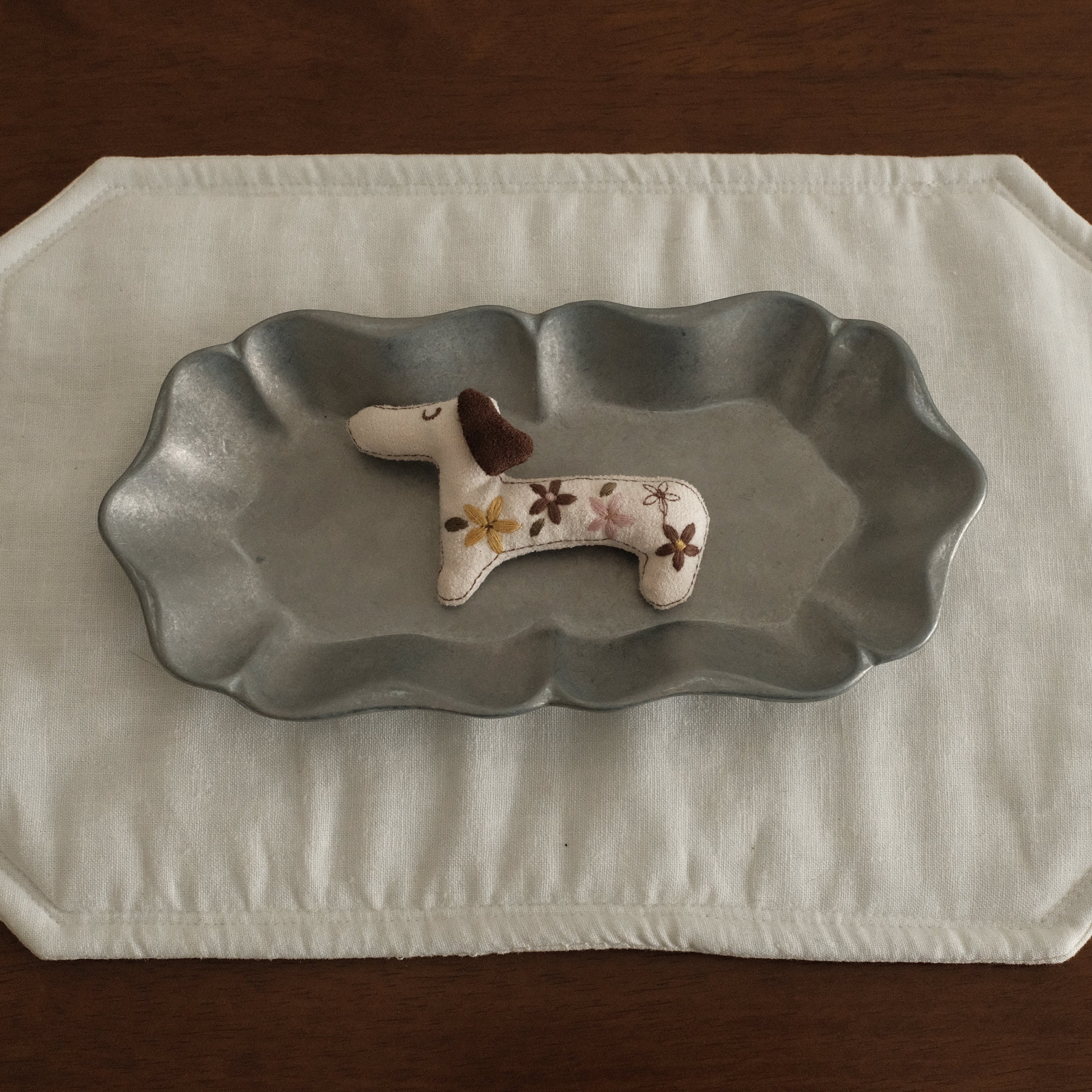 Decorative dachshund dog figurine brooch on a grey metal dish plate with a white placemat 