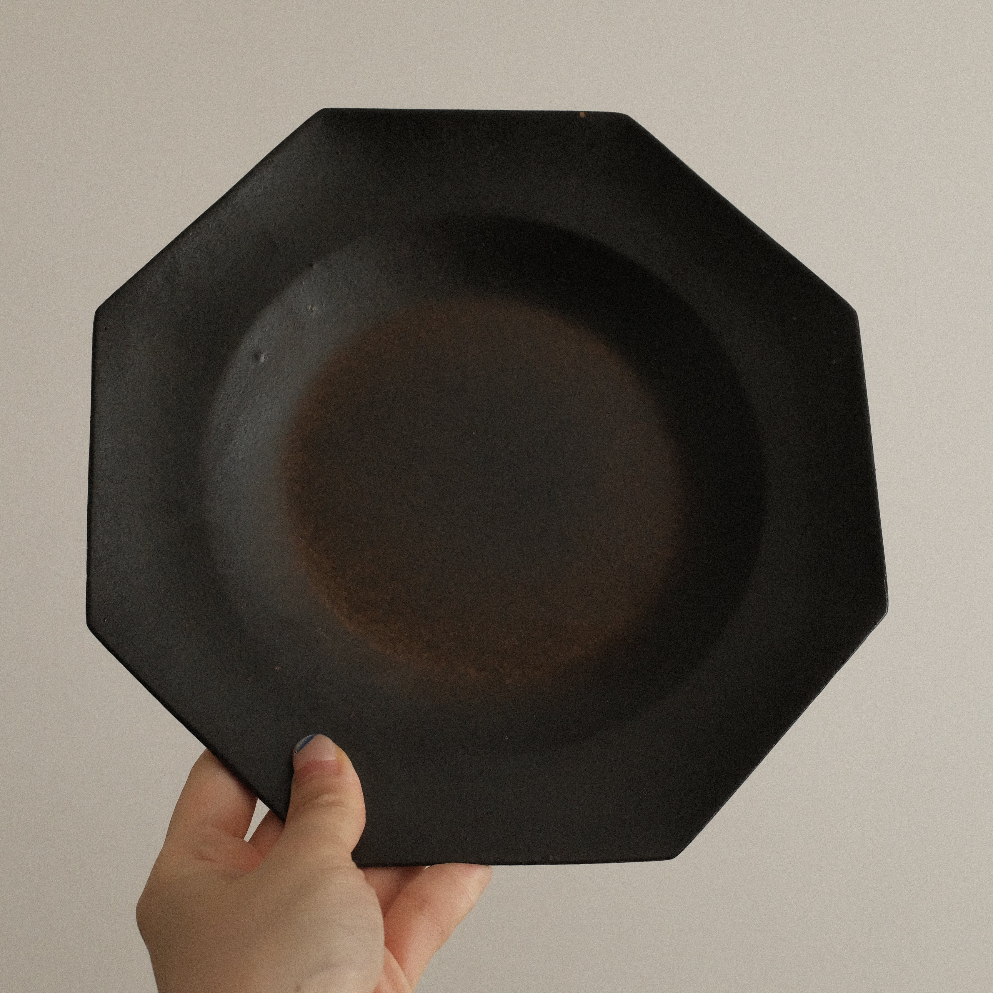 Black octagonal plate held by a hand against a beige background