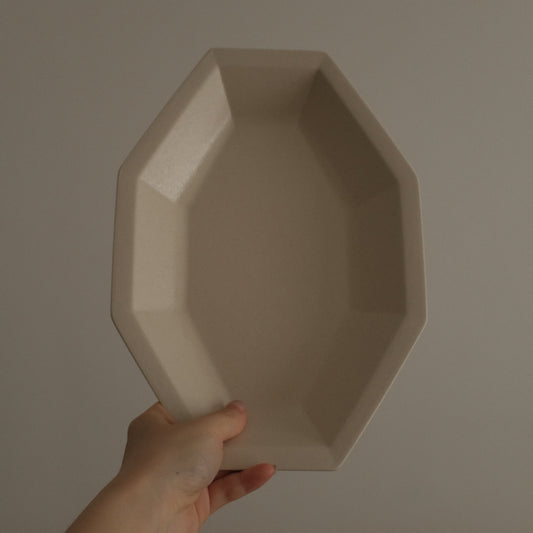 Hand holding a geometrically octagonal shaped beige ceramic plate against a plain background