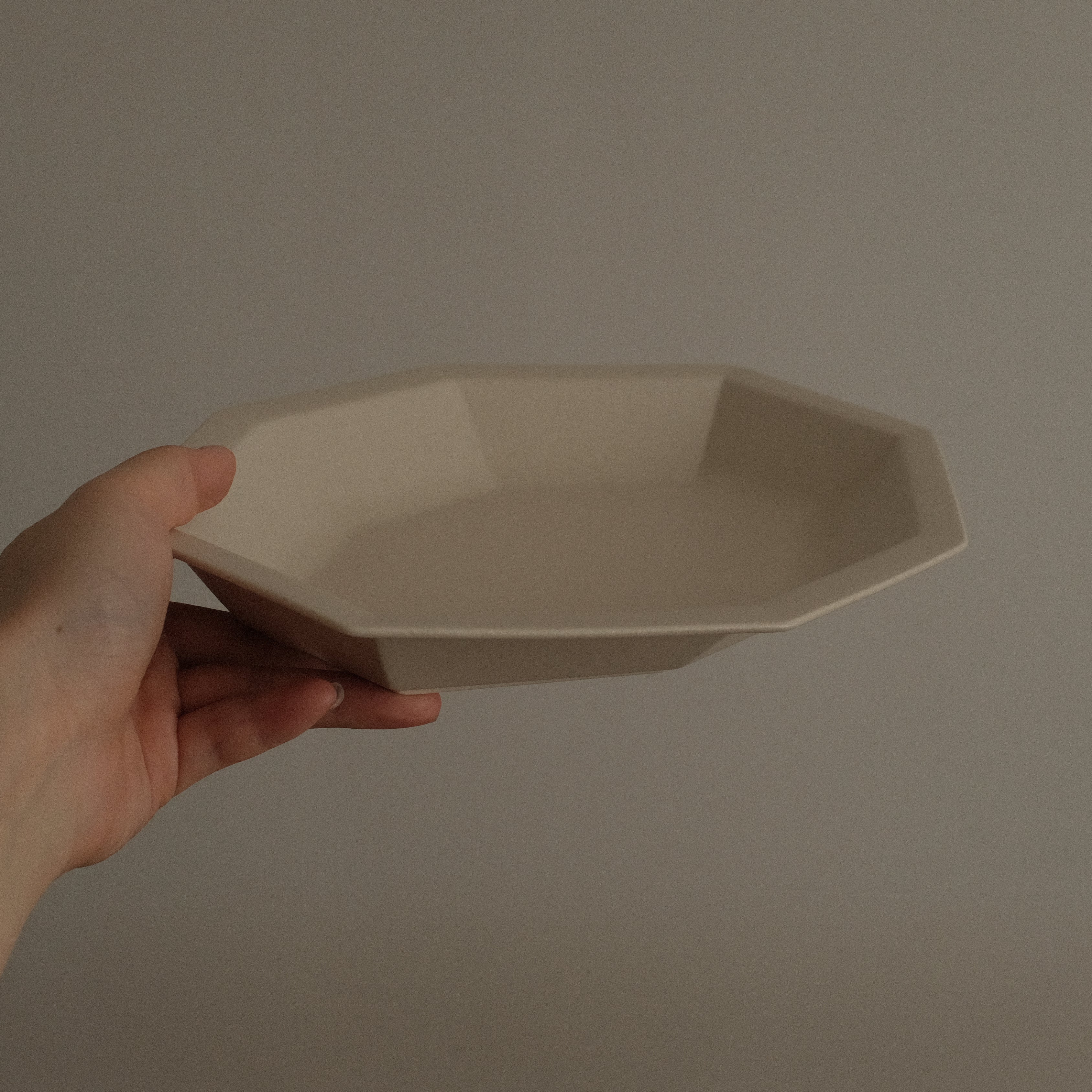 Hand holding a beige ceramic plate against a plain background