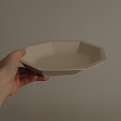 Hand holding a beige ceramic plate against a plain background