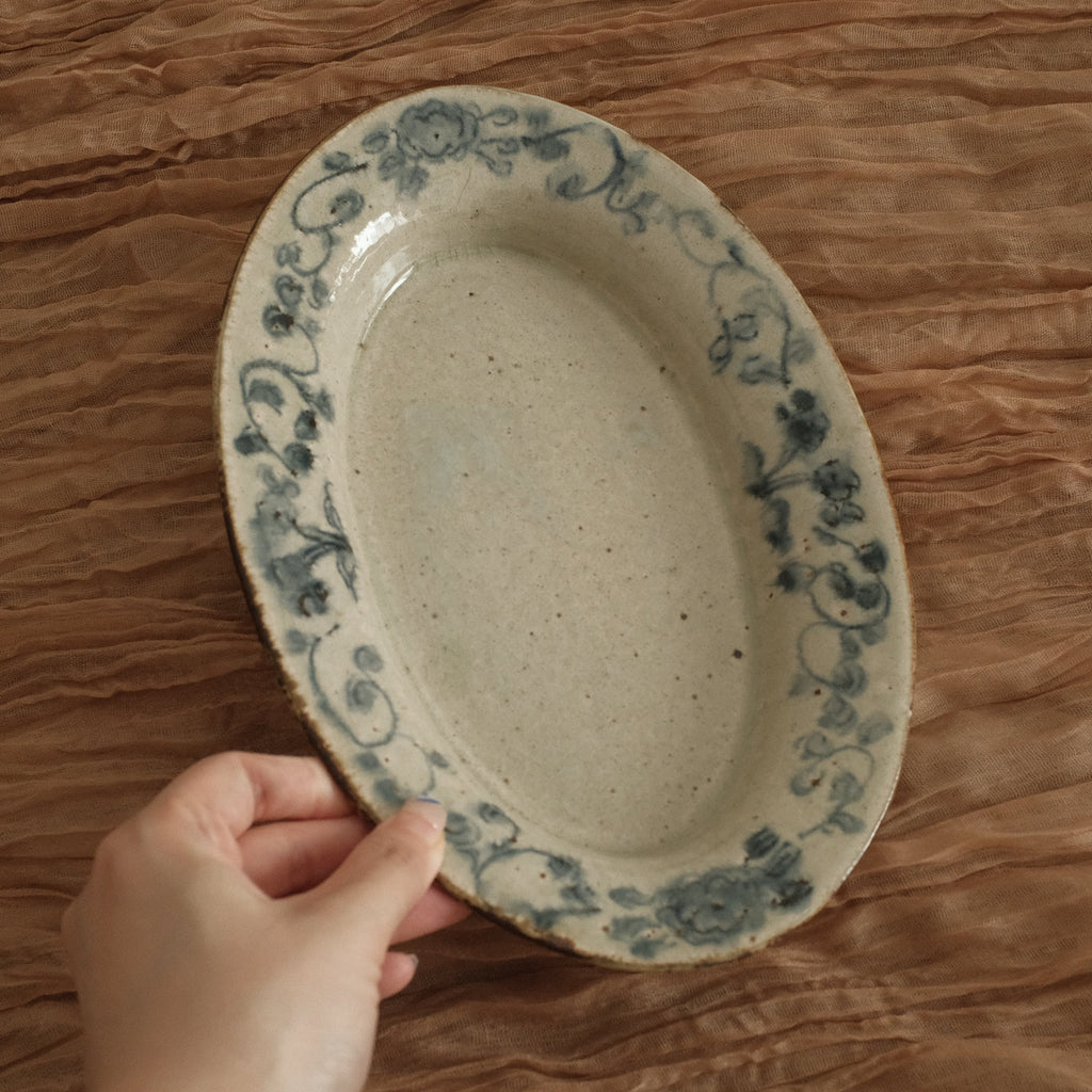 Hand holding a ceramic plate with floral patterns on a textured brown surface