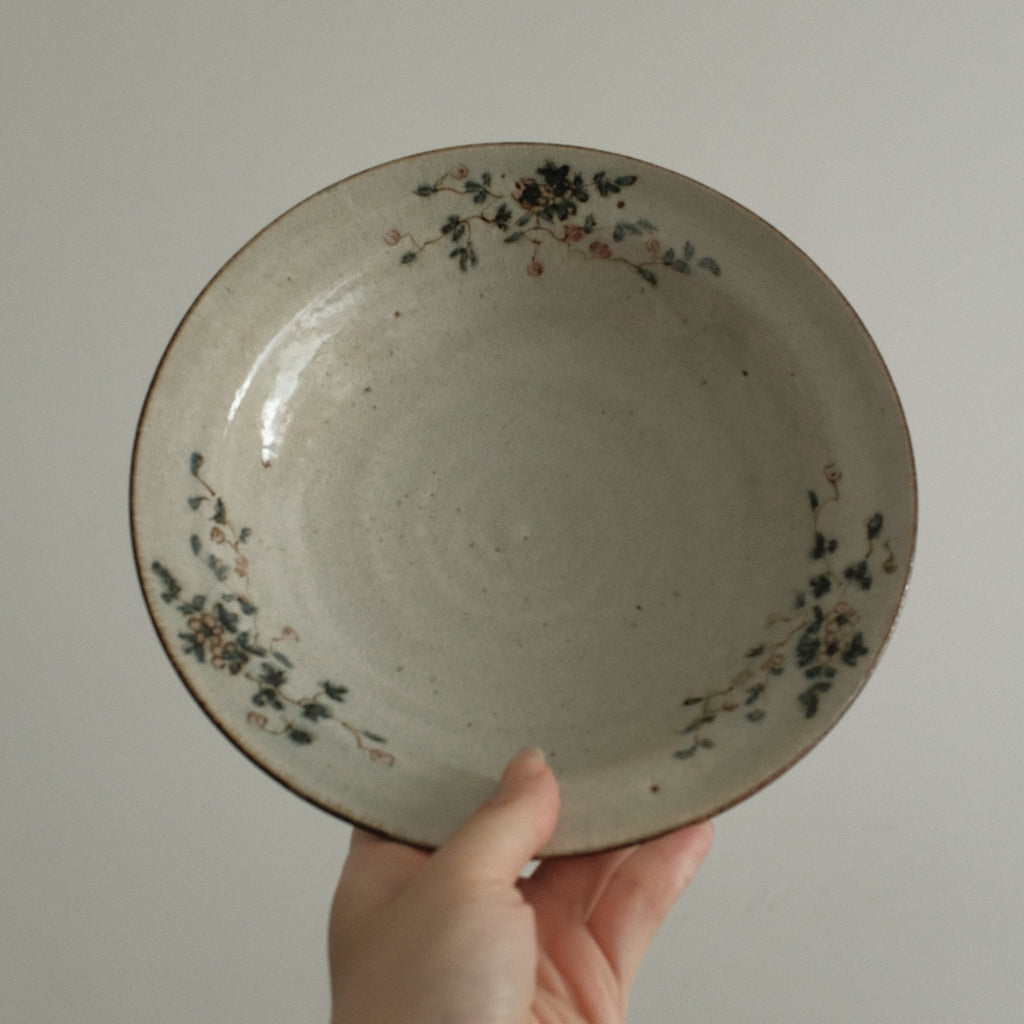 Ceramic plate with floral patterns held by a hand against a plain background