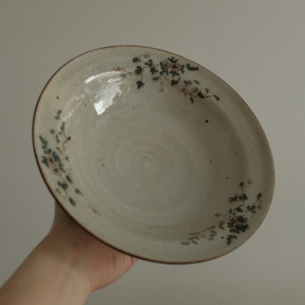 Hand holding a ceramic plate with black specks against a plain background