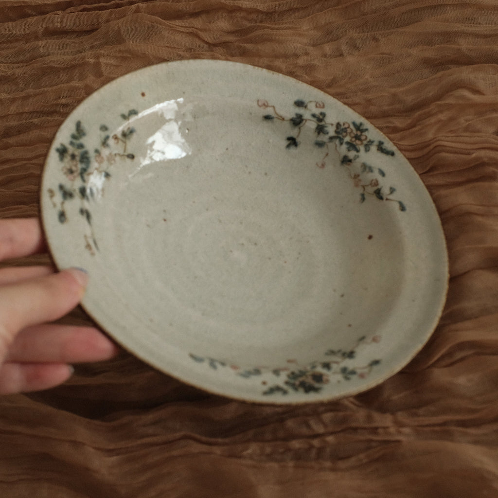 Hand holding a ceramic bowl with floral patterns on a brown textured surface