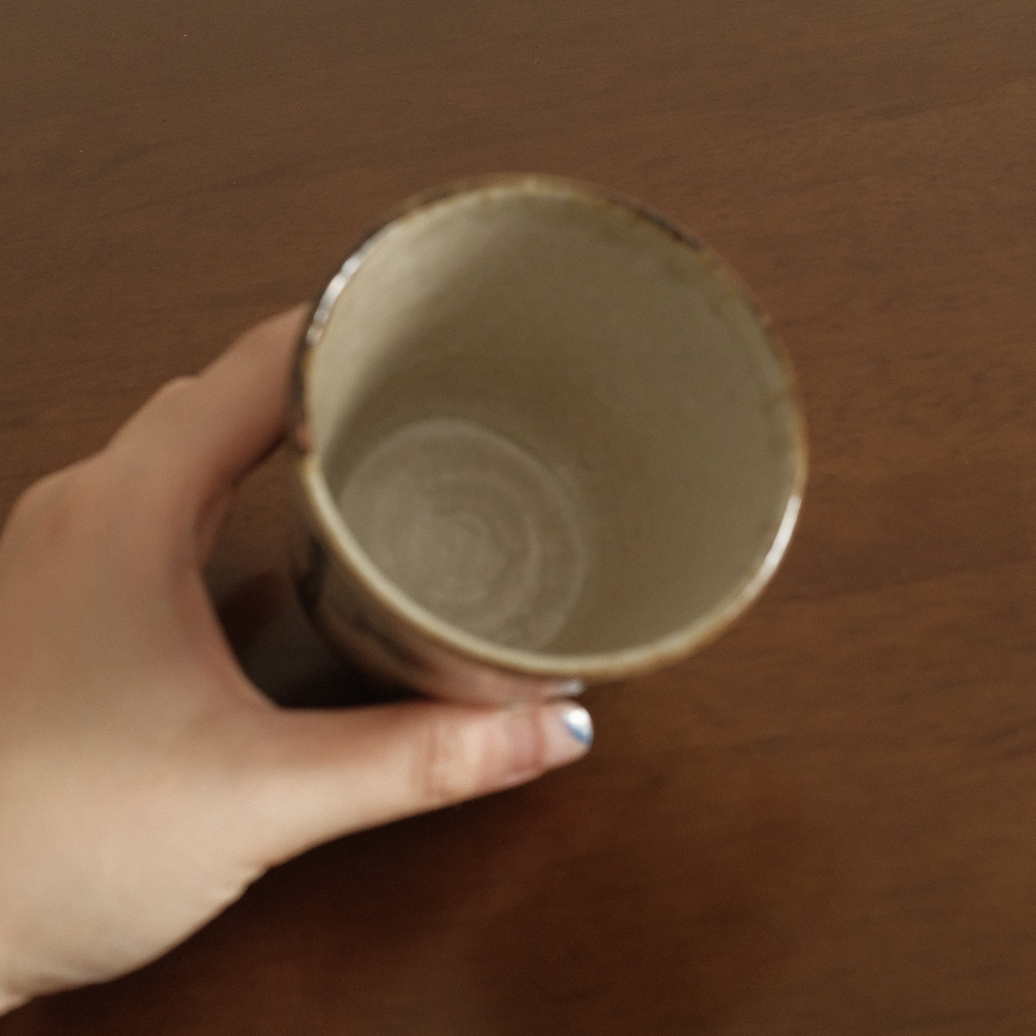 Hand holding a ceramic cup on a wooden surface