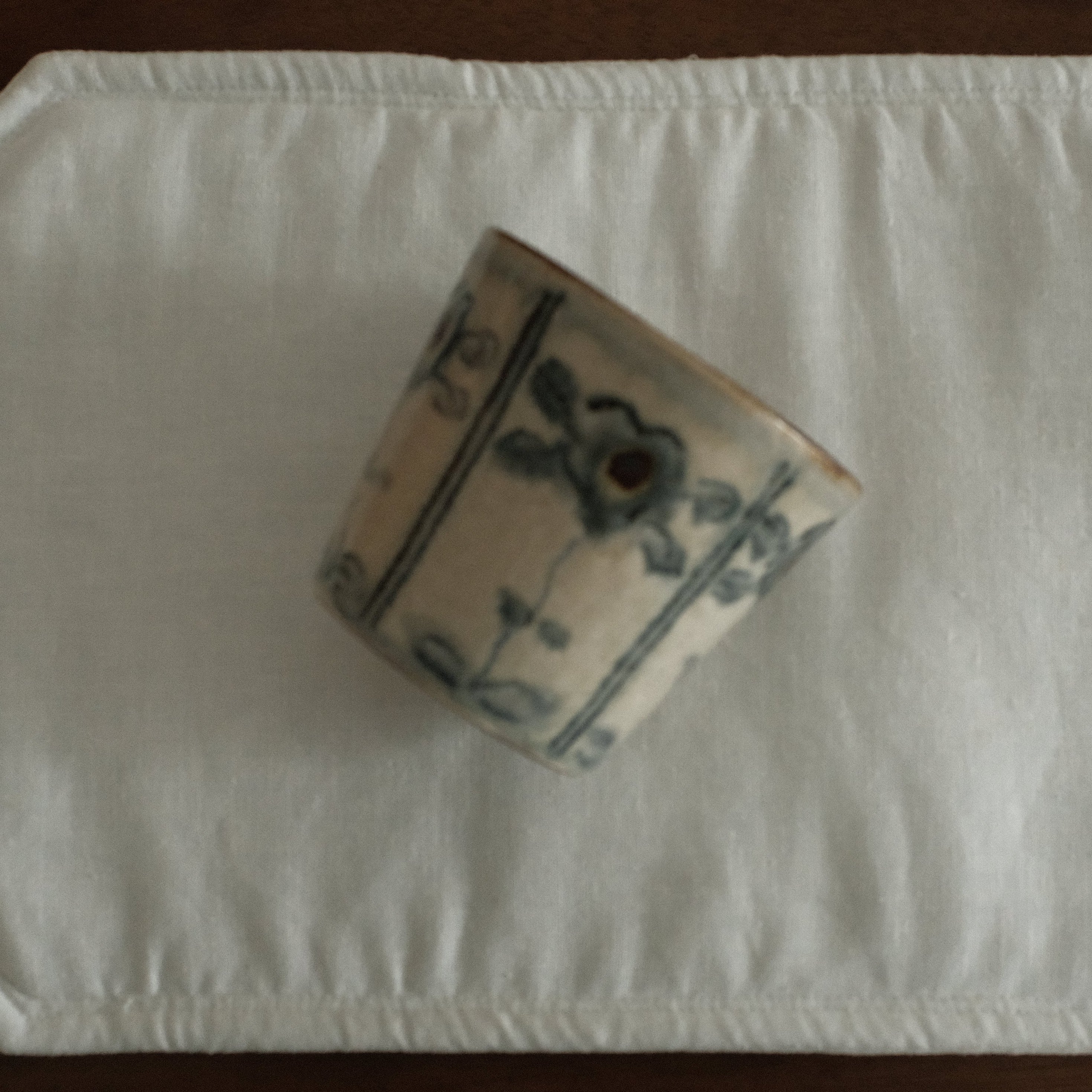 Decorative floral pattern cup with blue patterns on a white rectangular mat on a wooden surface
