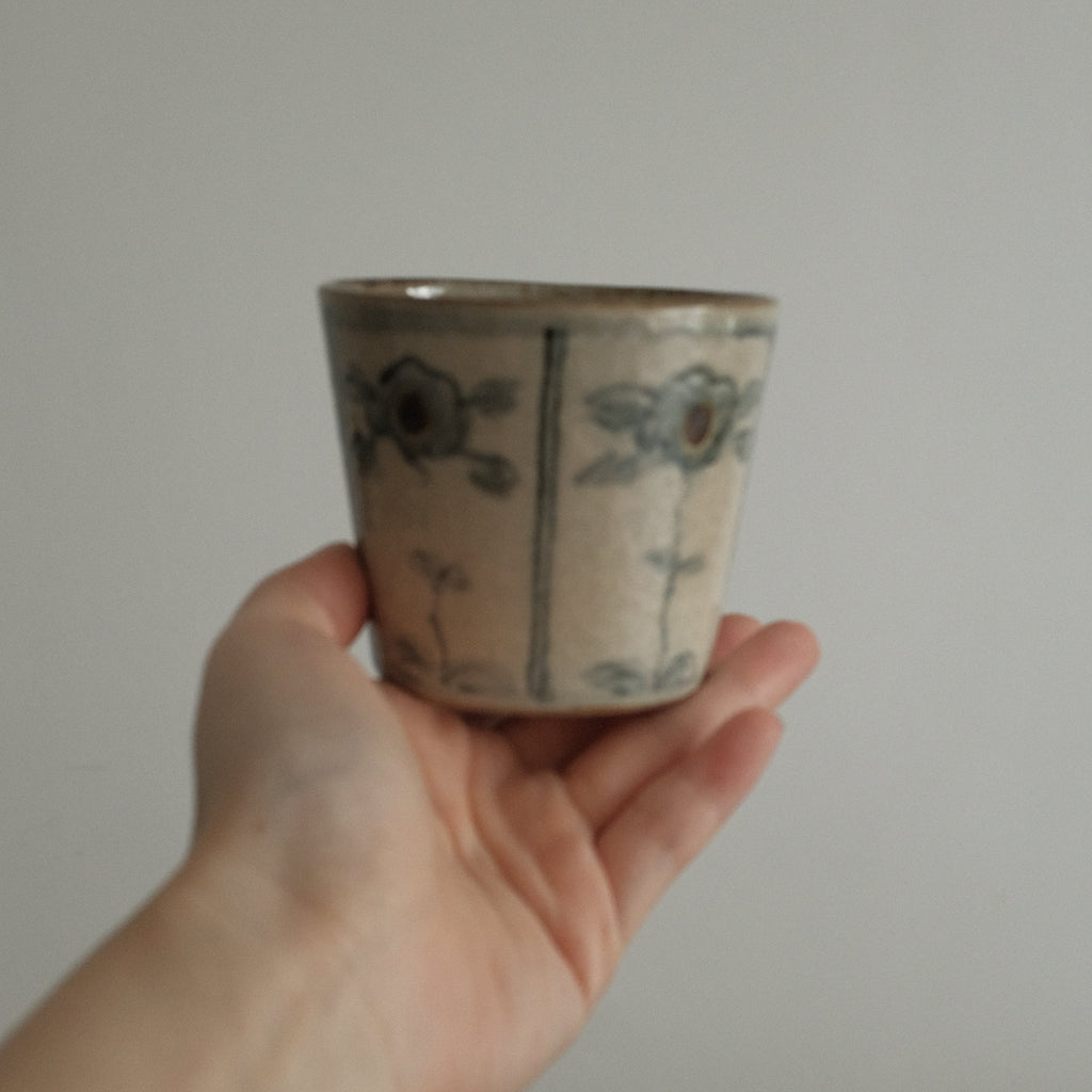 Hand holding a small ceramic cup with floral patterns against a plain background