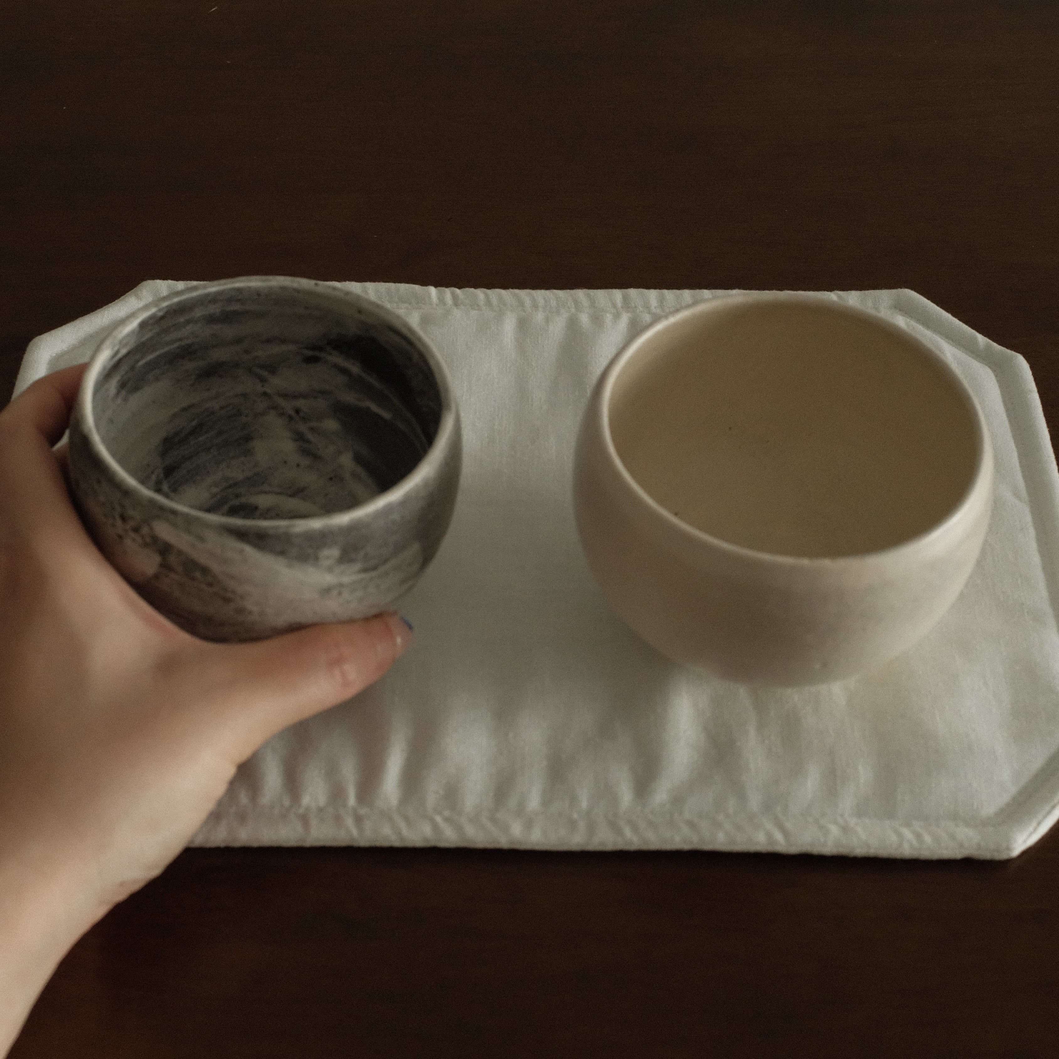 Two ceramic bowls on a white tray held by a hand against a dark background