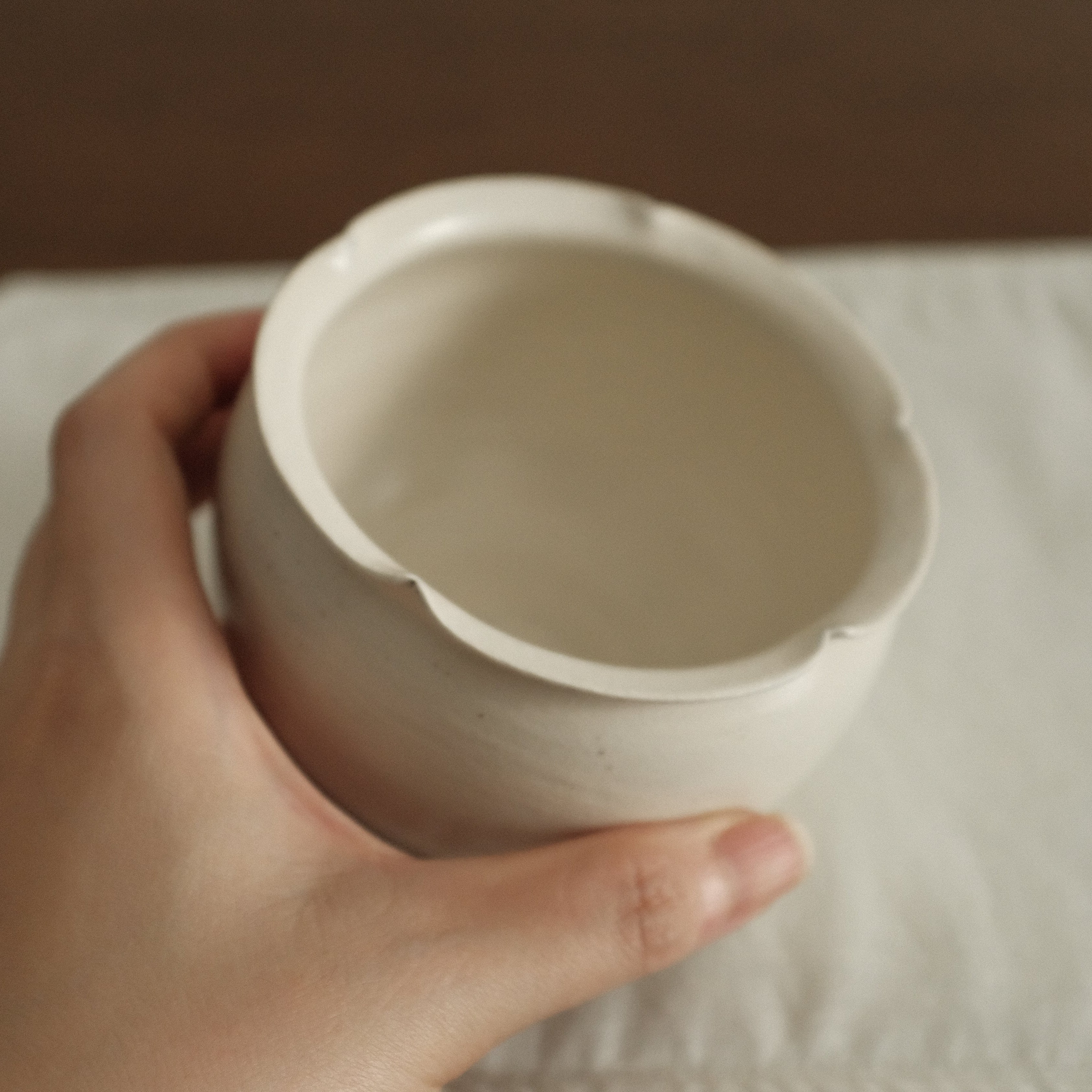 Hand holding a white ceramic cupon a neutral background
