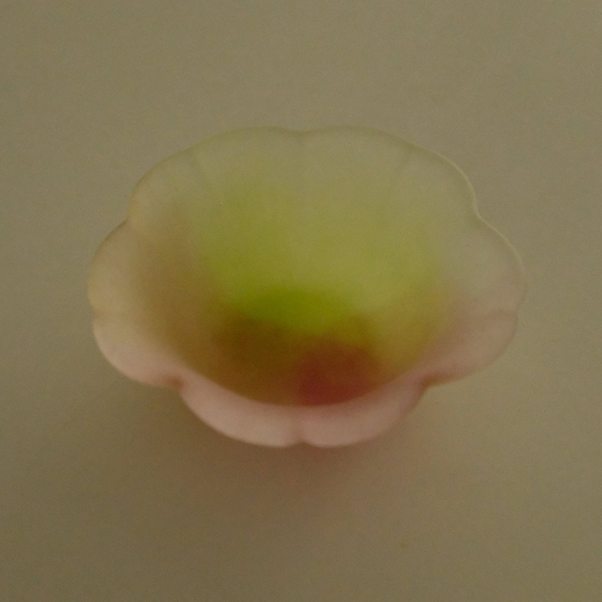 A small translucent flower-shaped bowl or cup with a scalloped rim, shown from above on a plain beige background.