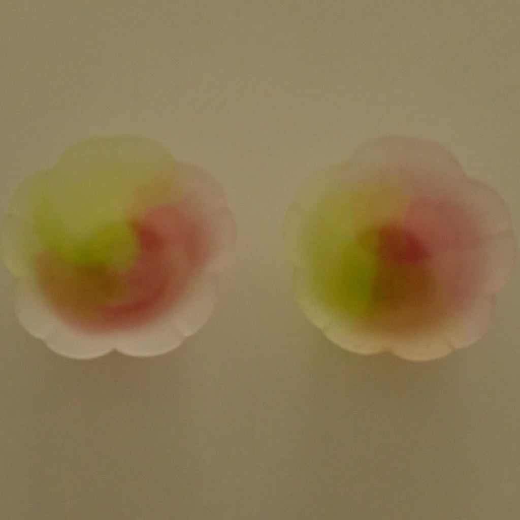 A pair of small flower-shaped stud earrings with a translucent design, featuring a blend of yellow-green and pink colors, shown against a plain beige background.