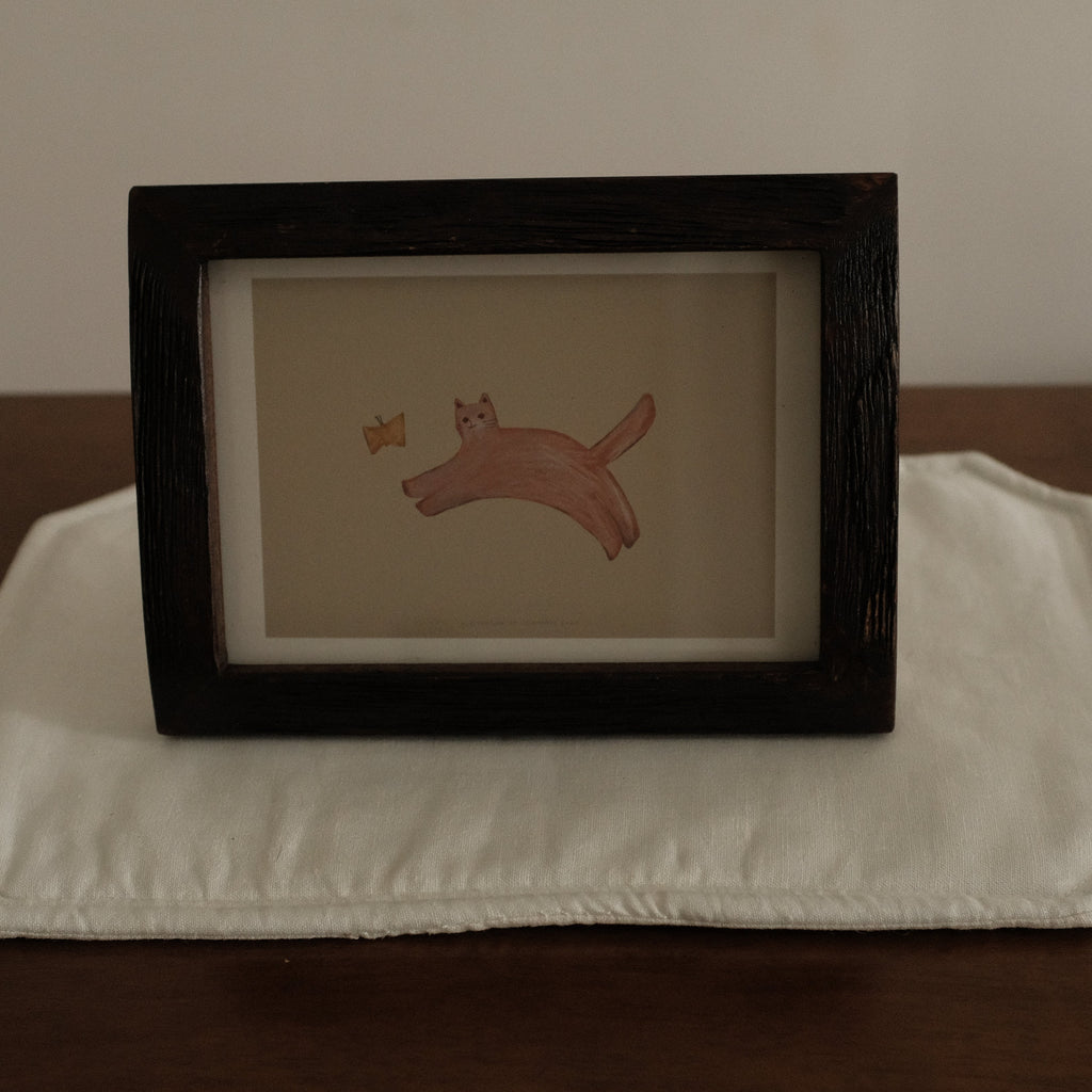 Framed artwork of a cat with butterfly on a white placemat with a brown background