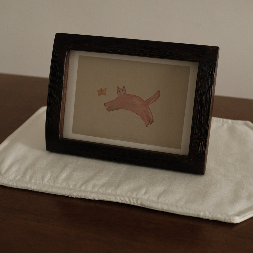 Framed artwork of a cat with butterfly on a white placemat  with a brown background