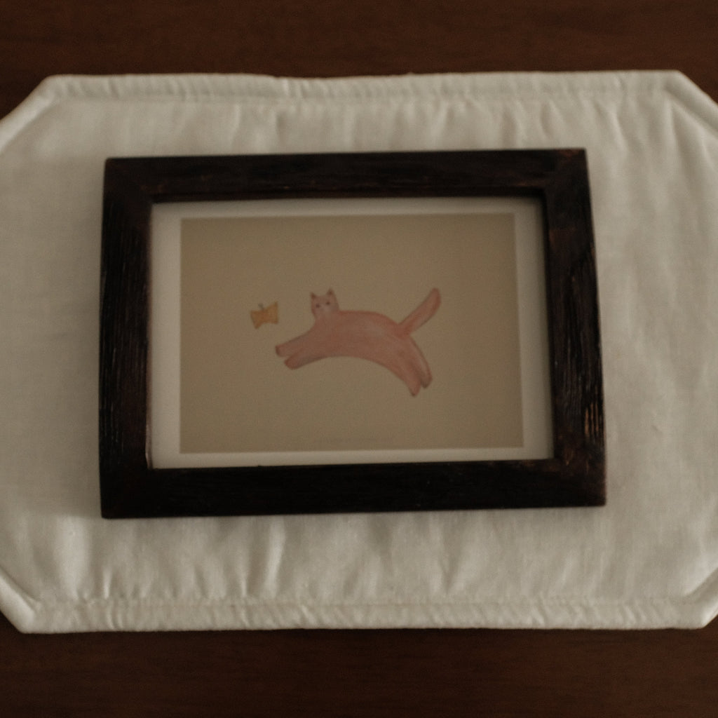Framed artwork of a cat with butterfly on a textured white surface with a dark brown background