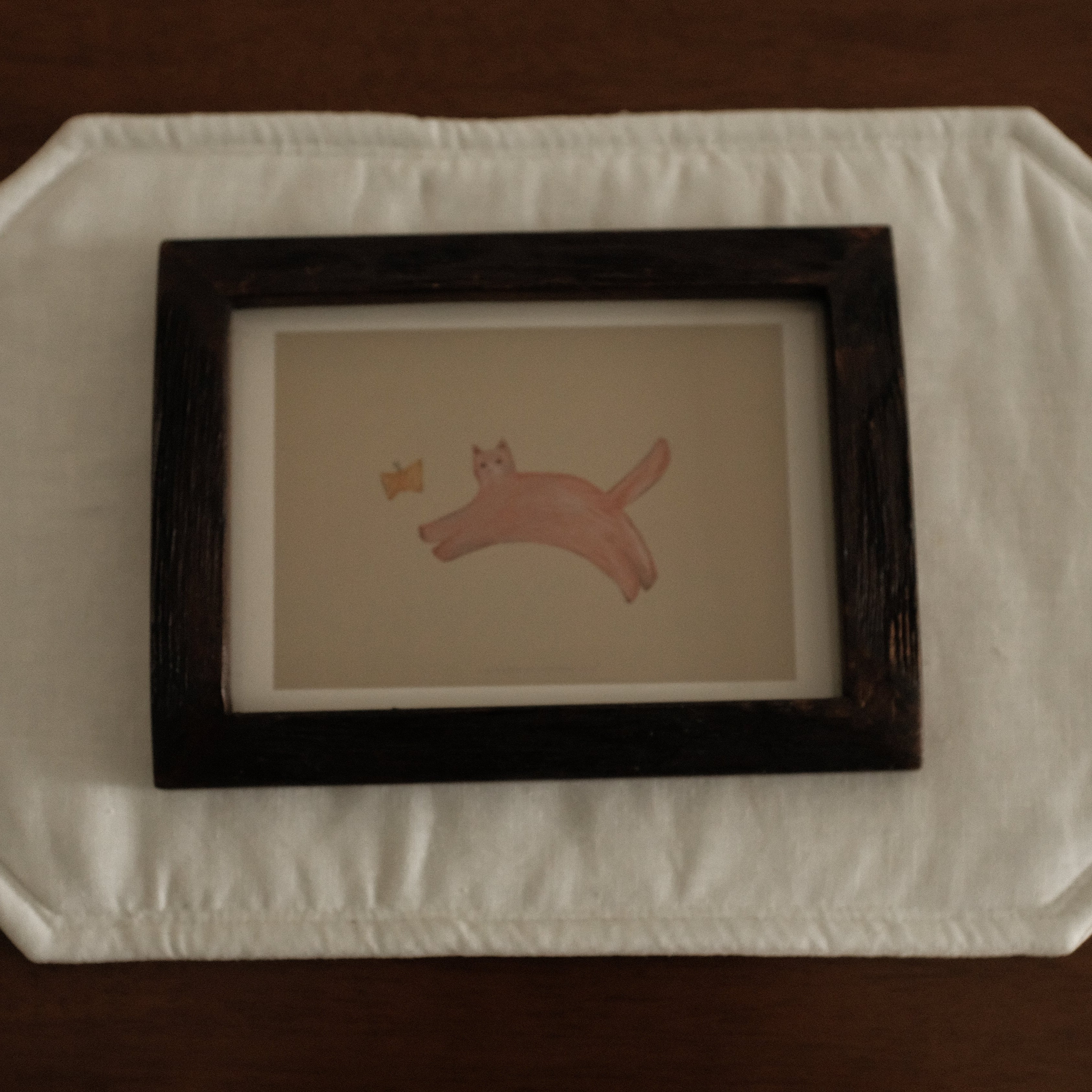 Framed artwork of a cat with butterfly on a textured white surface with a dark brown background