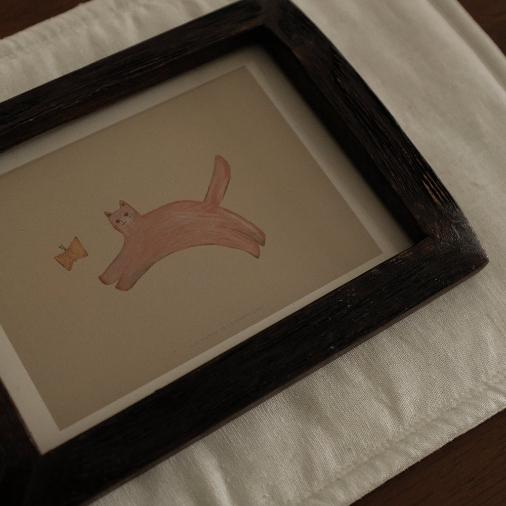 Framed illustration of a pink cat with a butterfly on a white surface