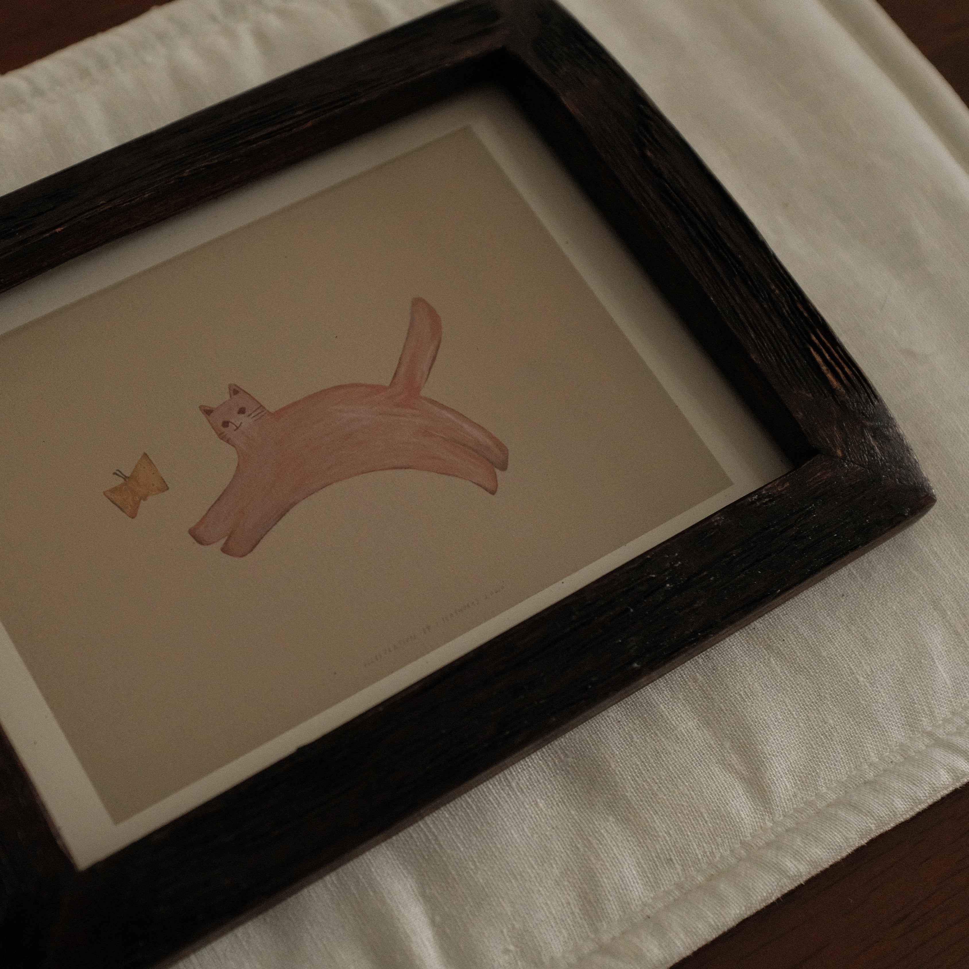 Framed illustration of a pink cat with a butterfly on a white surface