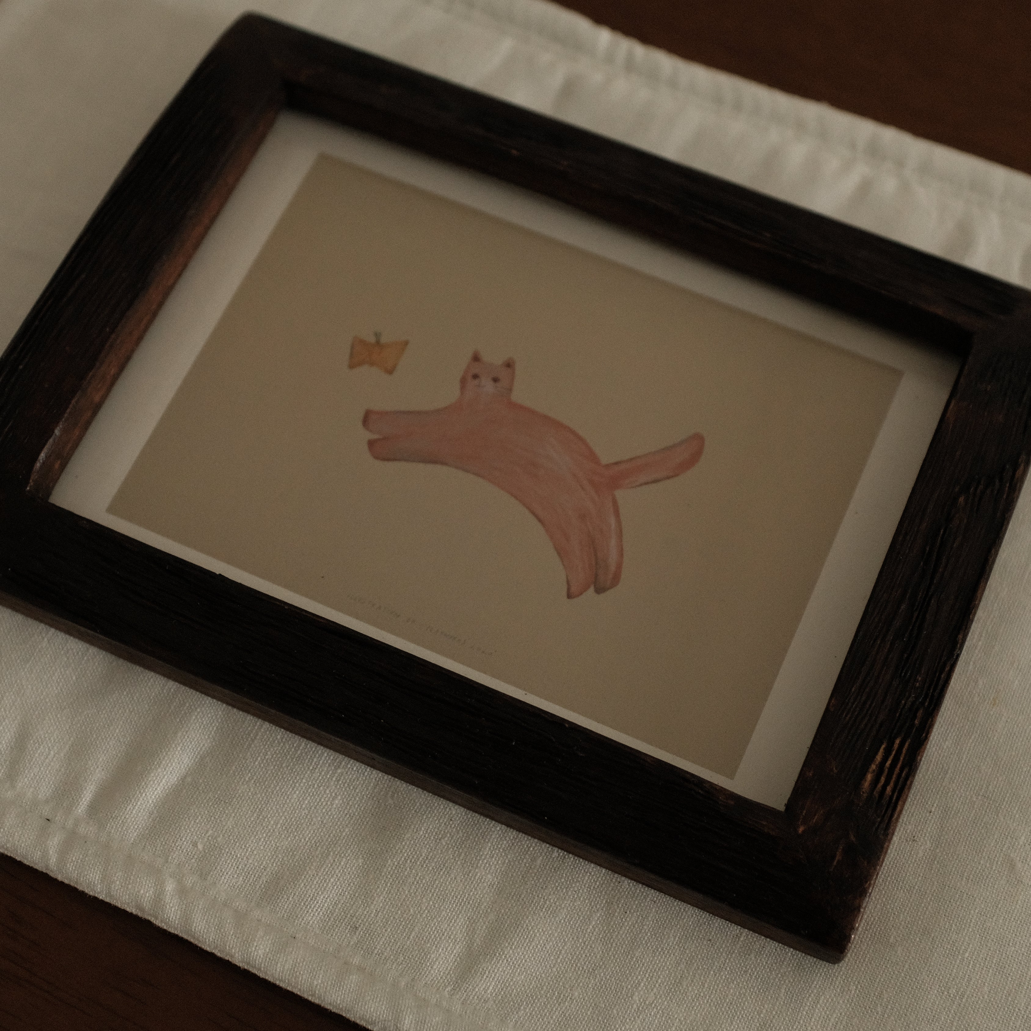 Framed drawing of a cat with butterfly on a white surface