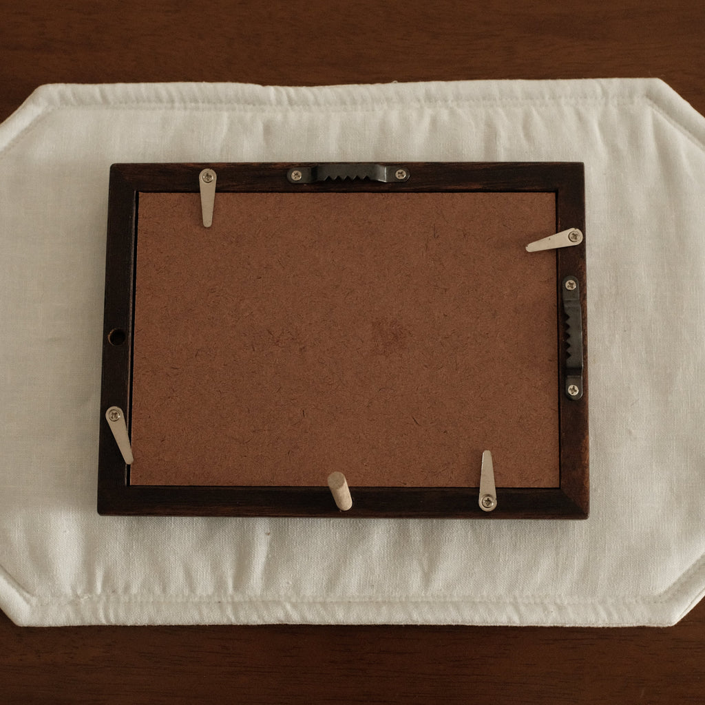 Rectangular brown frame on a white mat with clips, placed on a wooden surface.