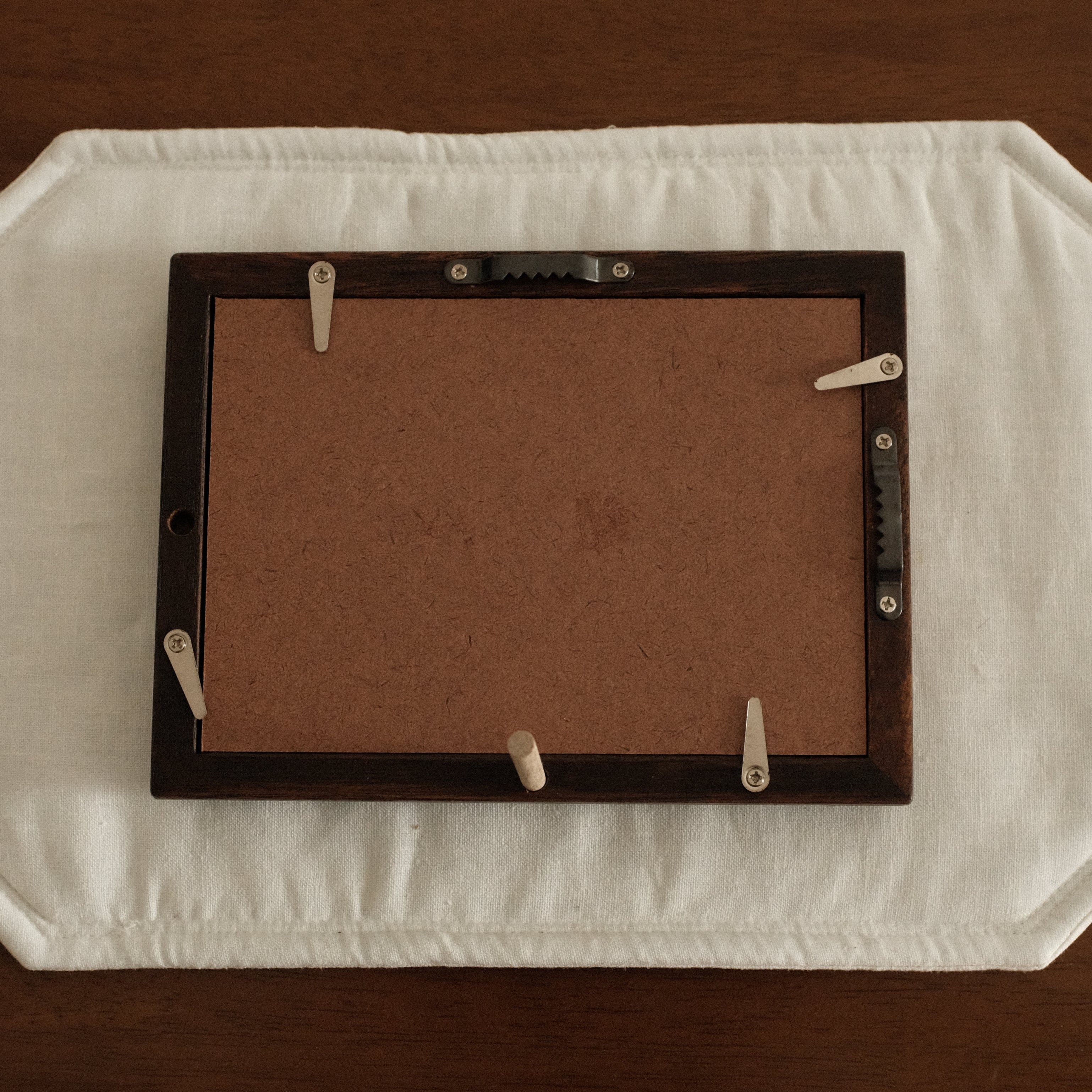 Rectangular brown frame on a white mat with clips, placed on a wooden surface.