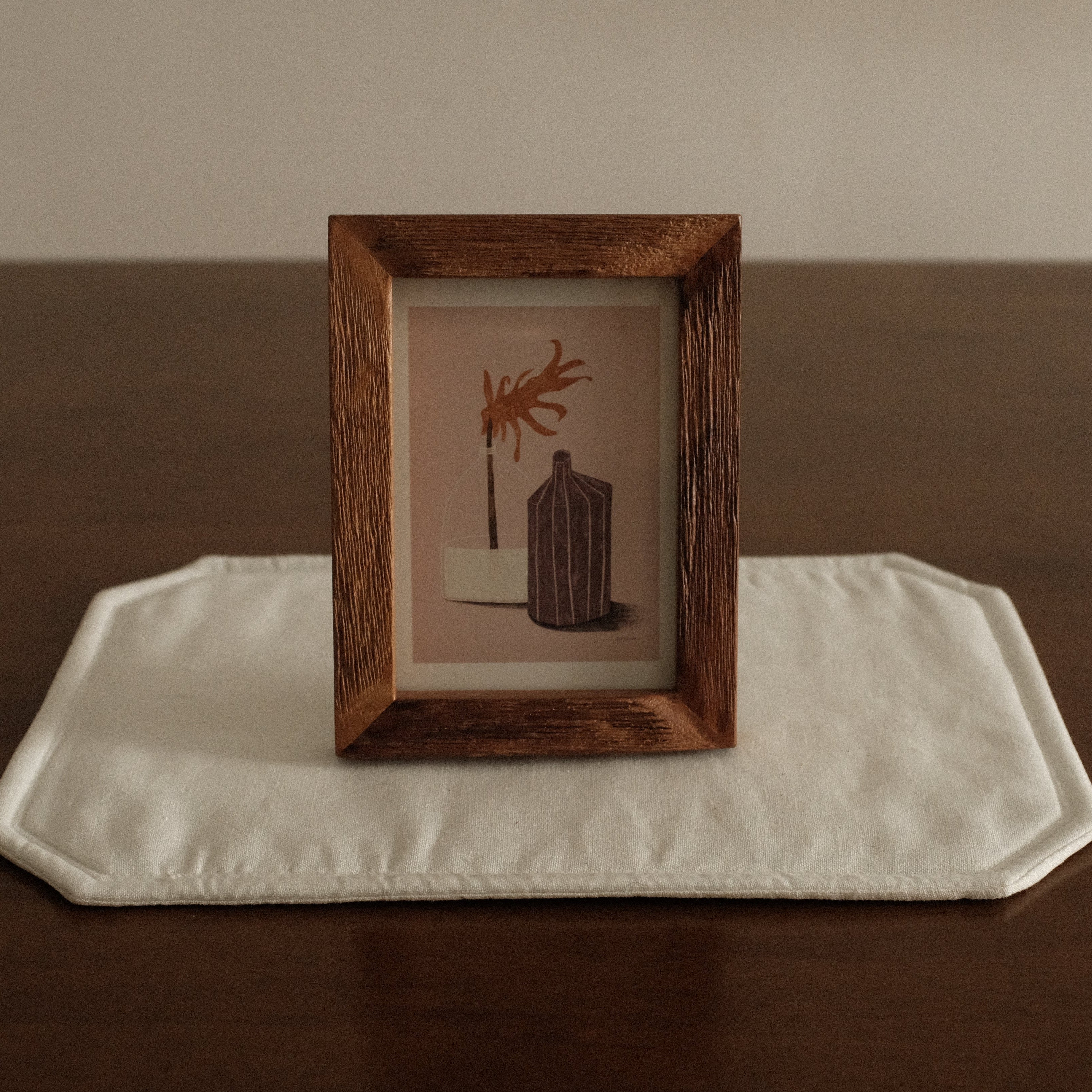 Wooden frame with a small painting on a white cloth on a wooden surface