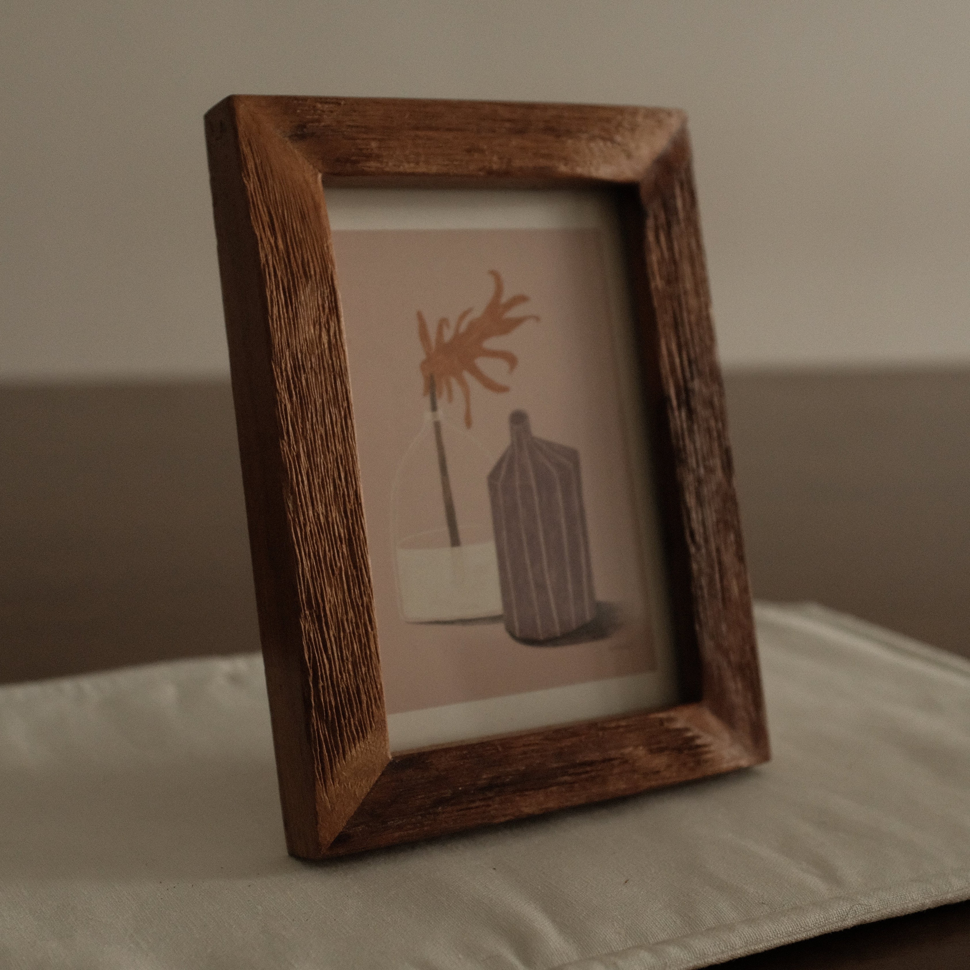 Wooden picture frame with a small painting inside on a white surface.