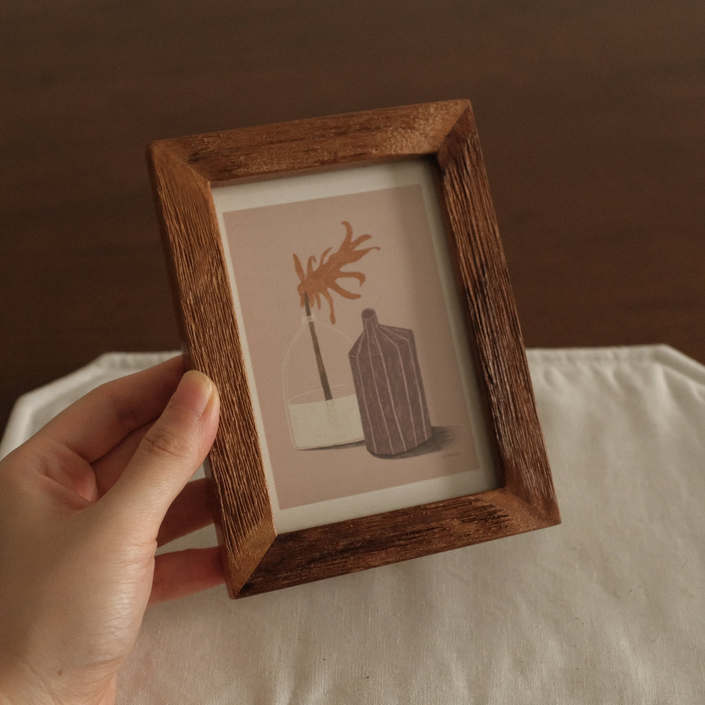 Hand holding a wooden-framed artwork with minimalistic design on a brown background
