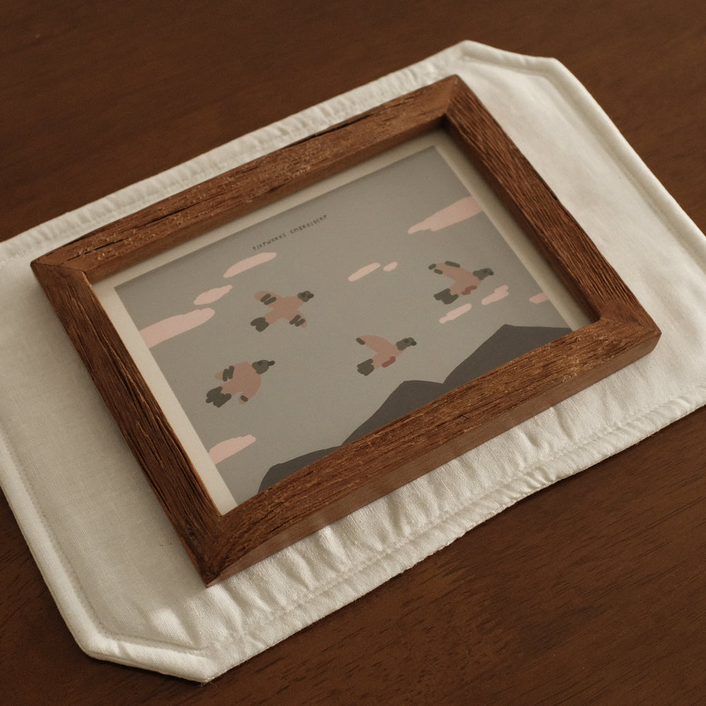 Teak Wooden picture frame with a small painting on a white decorative placemat on a wooden surface